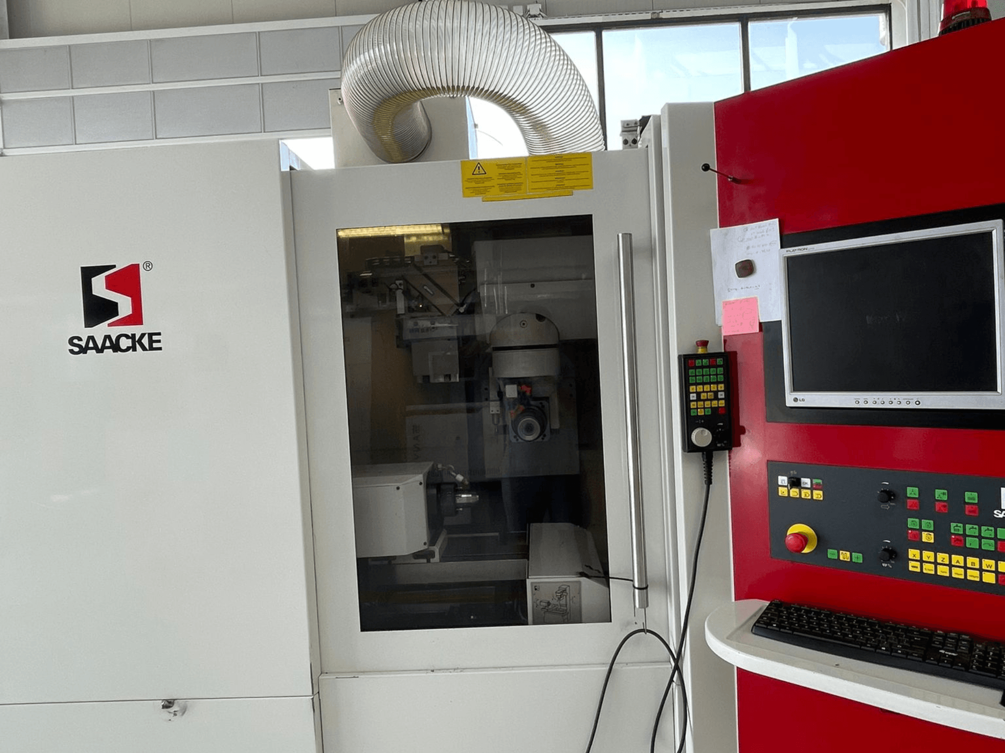 Stroj SAACKE v bílé a červené barvě, pohled zepředu, s ovládacím panelem, monitorem a viditelnými vnitřními částmi přes sklo.