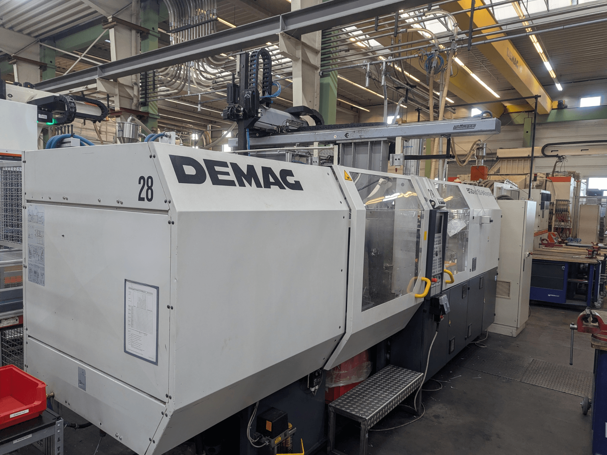 Pohled zepředu na hydraulický vstřikovací stroj DEMAG ERGOTECH 1500-840, který ukazuje ovládací prvky a bezpečnostní prvky.