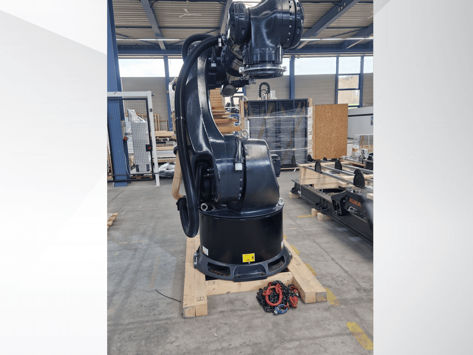 Robotické rameno KUKA KR 340 R3330 ve skladu, boční pohled znázorňující jeho základnu a kabely, s řetězy v popředí.