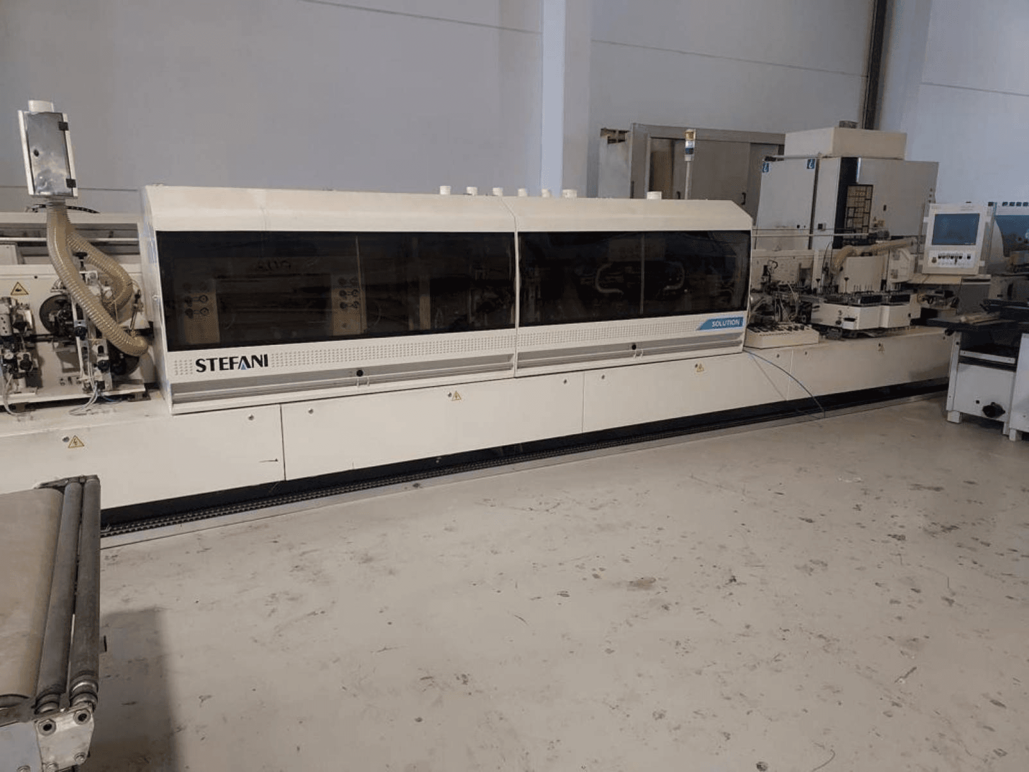 Olepovačka hran Stefani Solutions, pohled zepředu, s viditelným systémem odsávání prachu a ovládacím panelem, v dílně.