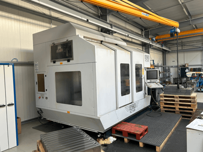 Stroj Spinner VC 1650 CNC, pohled zepředu, s ovládacím panelem, velkými okny a paletami naskládanými poblíž v dílně.