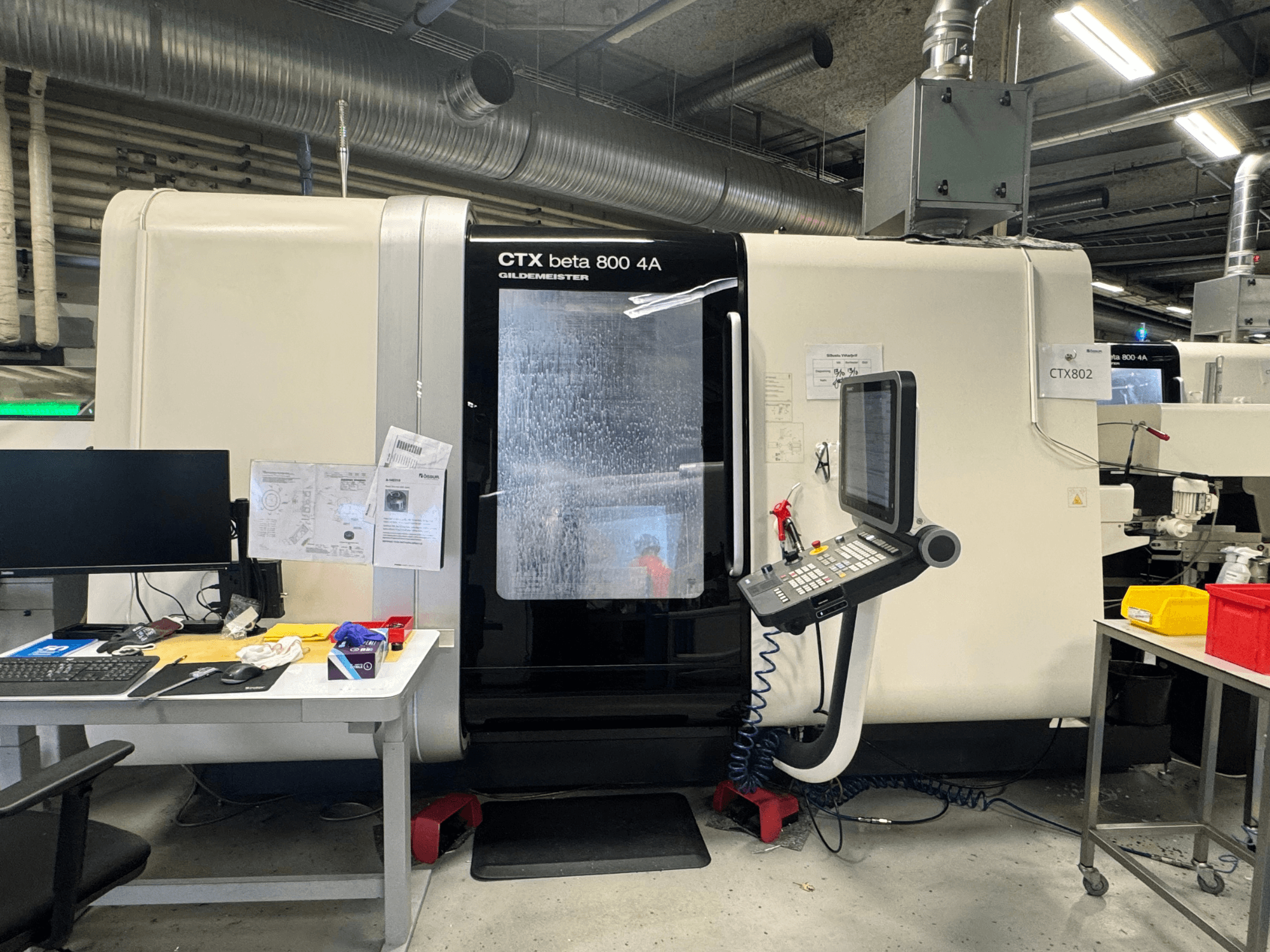 CNC stroj CTX beta 800 4A v dílně, boční pohled ukazuje ovládací panel a pracovní plochu přeplněnou nástroji a dokumenty.