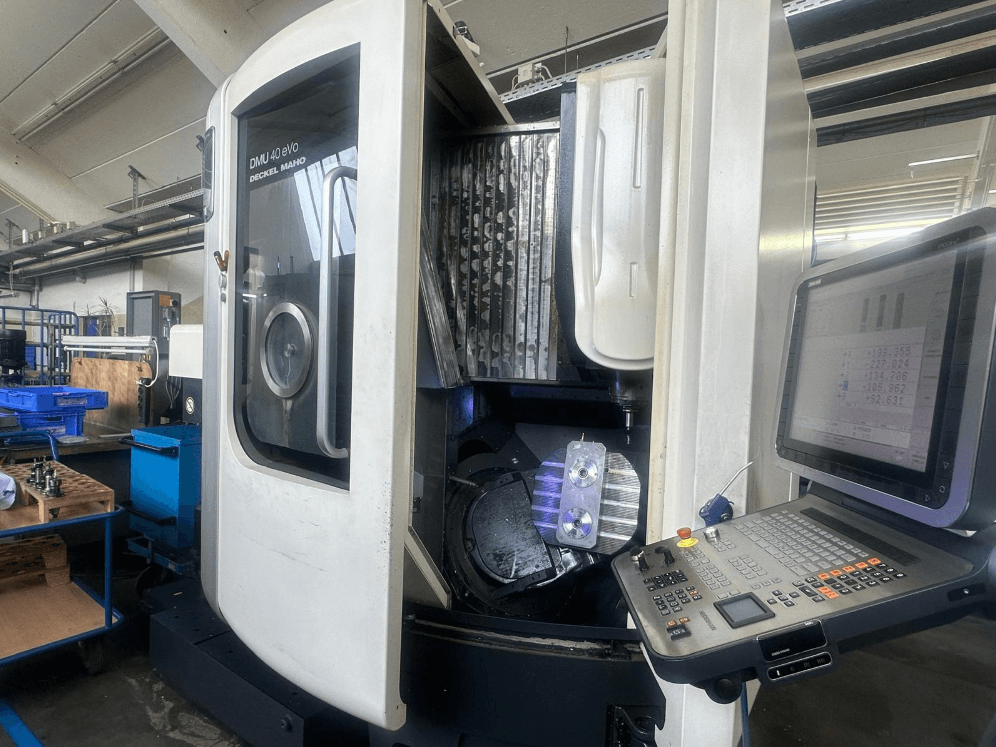 Frézka DMU 40 eVo od firmy Deckel Maho v dílně, pohled zepředu, ukazuje ovládací panel a kovový kus ve vřetenu.