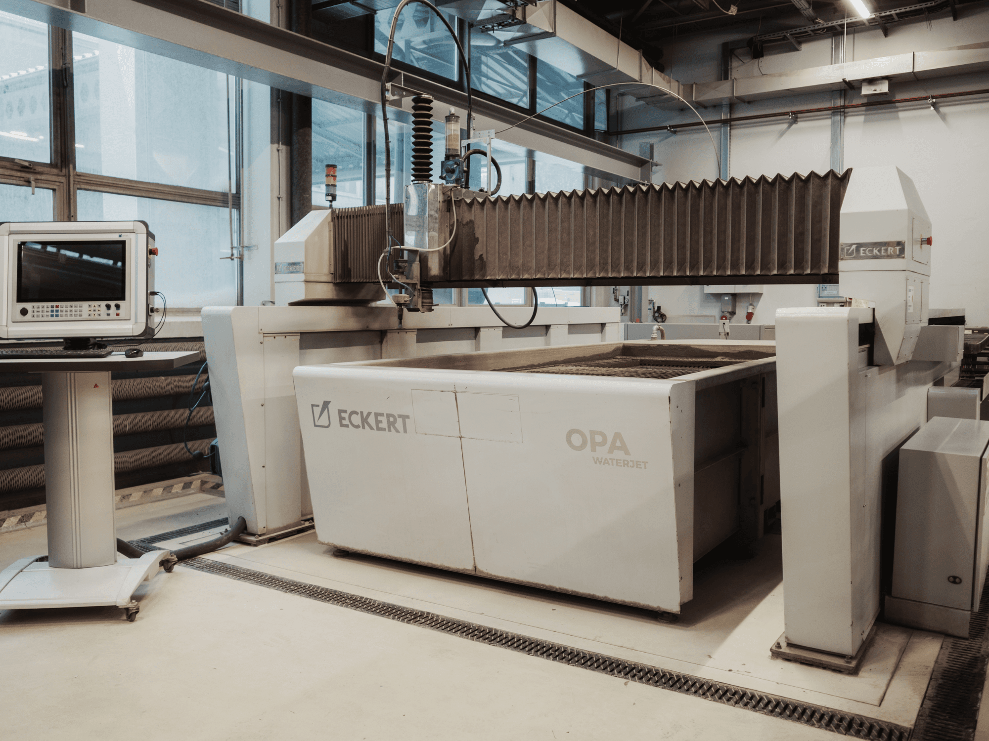 Řezací stroj ECKERT OPAL WATERJET v dílně, pohled zepředu s ovládacím pultem v blízkosti.