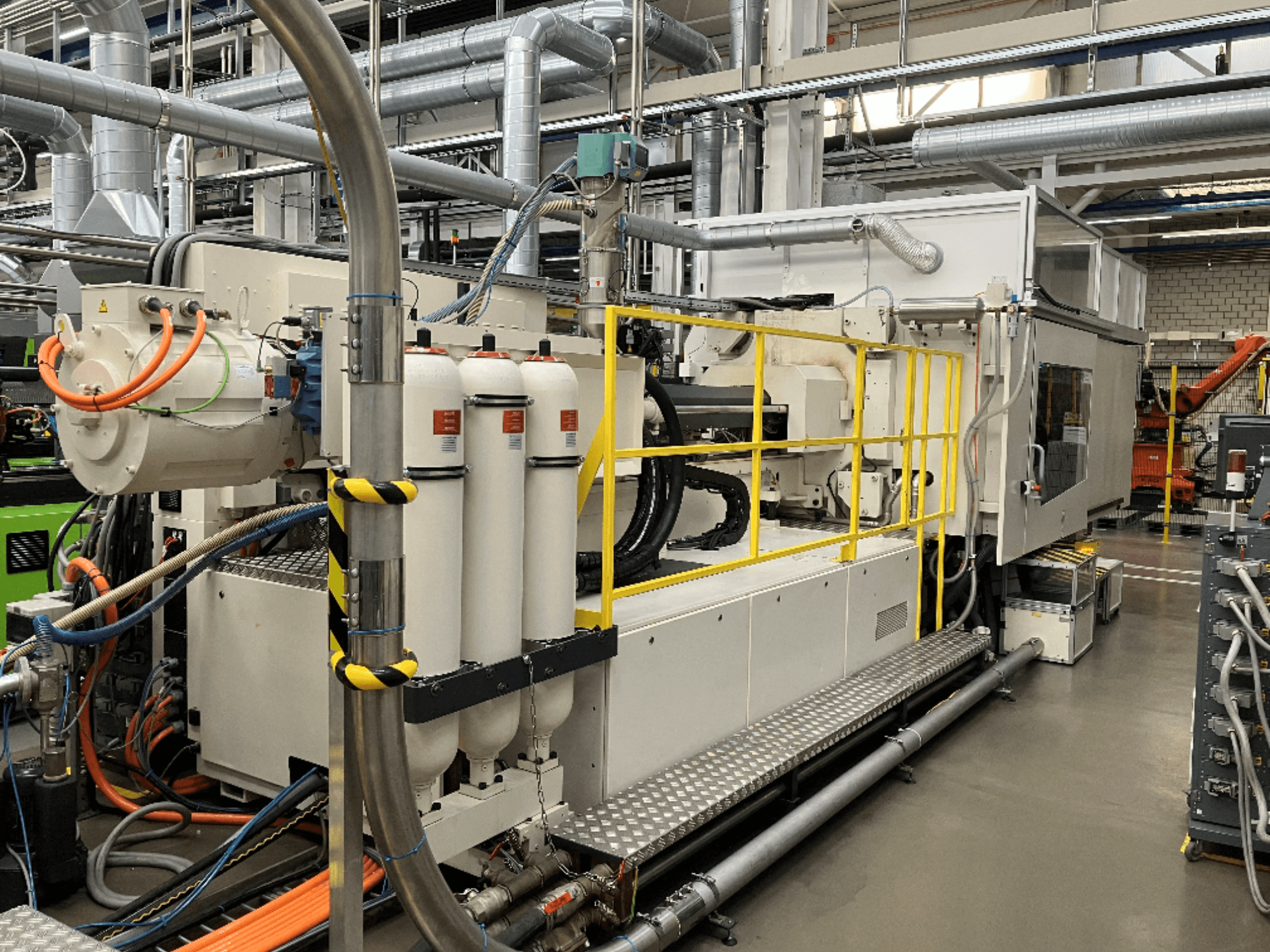 Průmyslový stroj s bílým a šedým pláštěm, několika hadicemi a filtračními nádržemi; boční pohled ukazuje provozní nastavení.