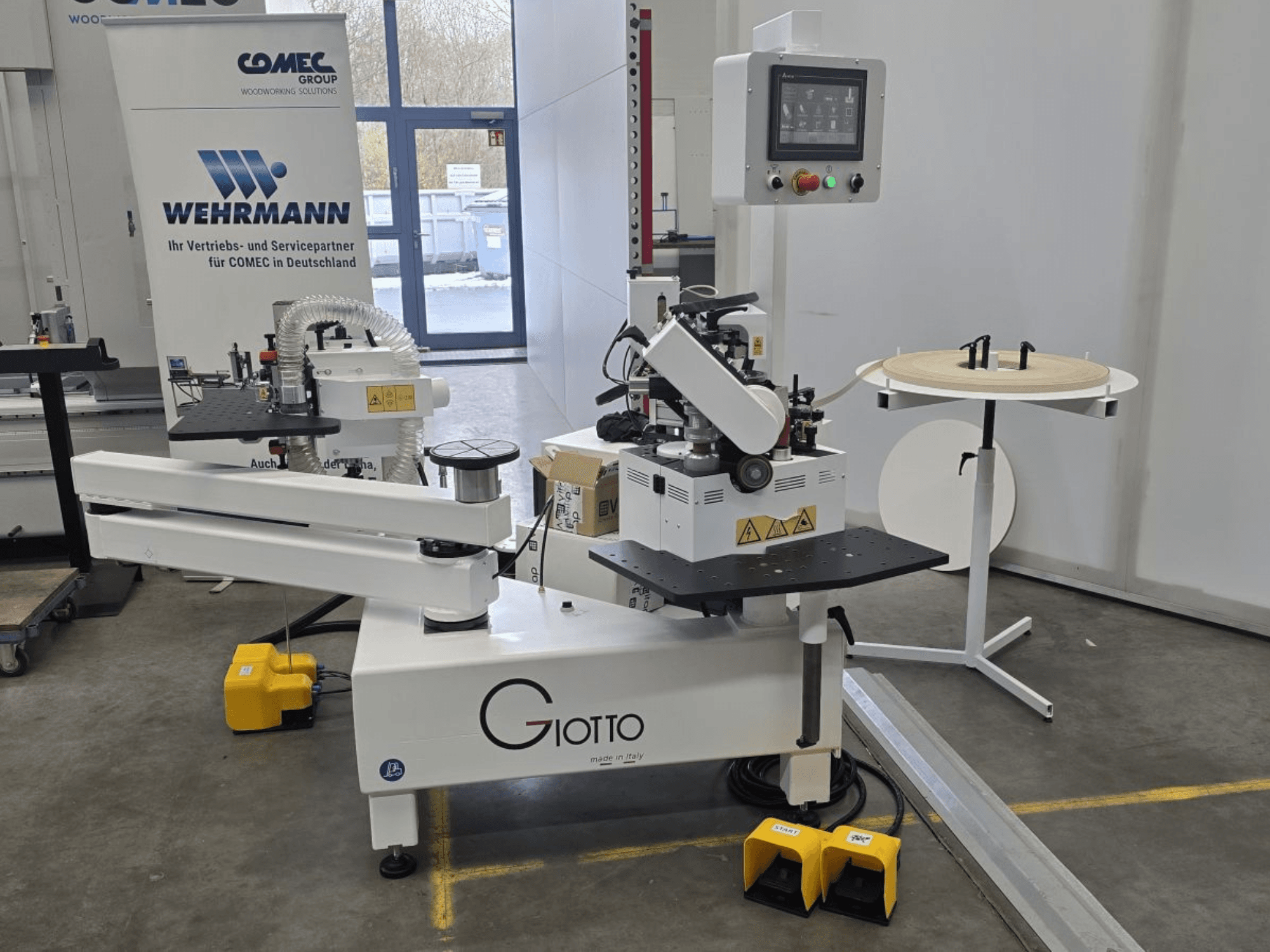 Stroj na zpracování dřeva Giotto s ovládacím panelem, pohled z boku, včetně nožních pedálů a otočné pracovní plochy.