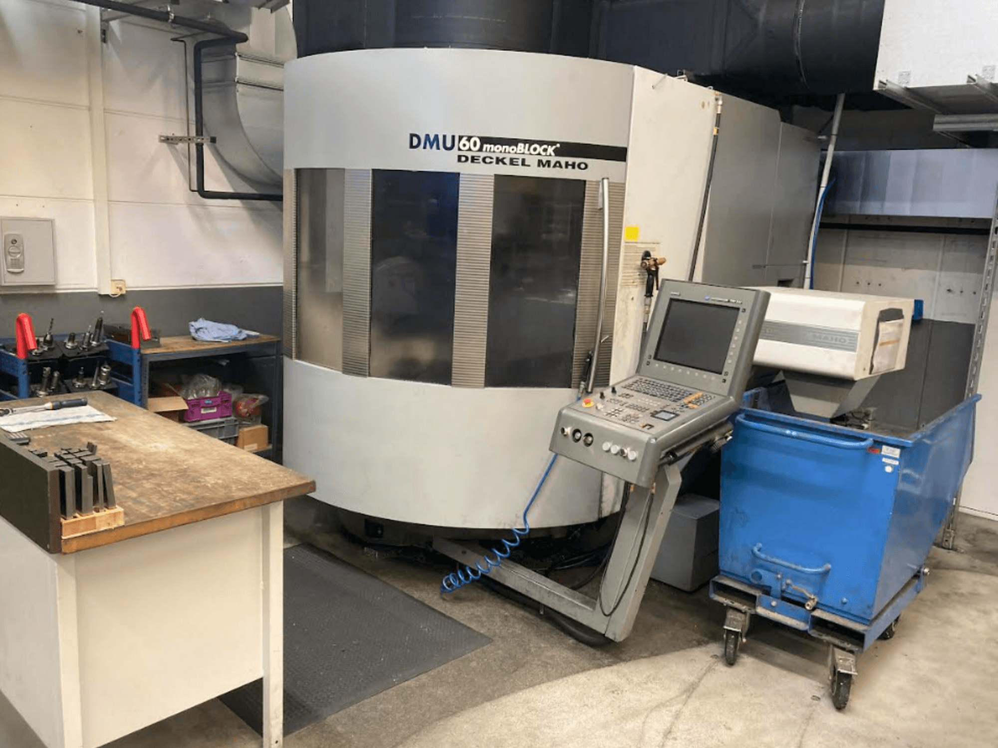 DMG MORI DMU 60 Monoblock vertikální obráběcí centrum, pohled zepředu s viditelným ovládacím panelem, pracovním prostorem a modrým vozíkem na nástroje.