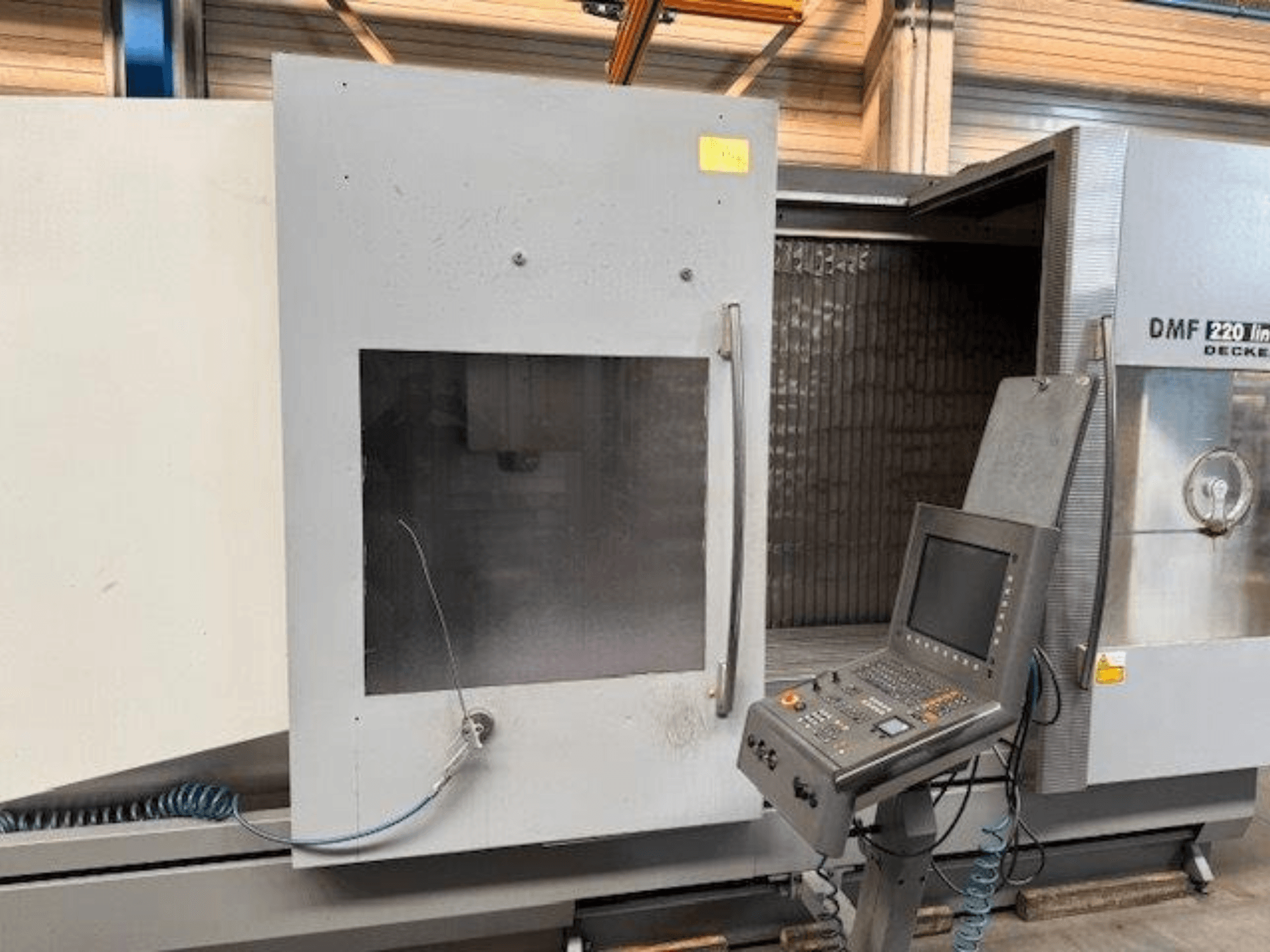 Pohled zepředu na lineární vertikální obráběcí centrum DECKEL MAHO DMF 220, na kterém je vidět ovládací panel a otevřené dveře stroje.