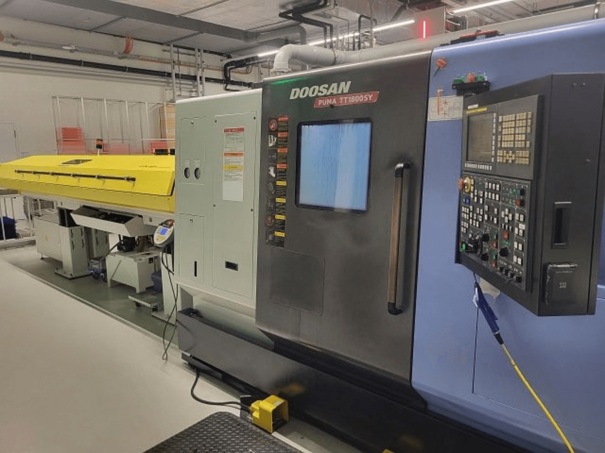 Obráběcí centrum DOOSAN PUMA TT 1800 SY, pohled zepředu s ovládacím panelem a žlutým krytem, průmyslové prostředí.