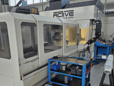 CNC stroj Active 3000 v dílně, pohled zepředu s nástroji na modrém vozíku, viditelné ovládací prvky a pracovní plocha uvnitř.