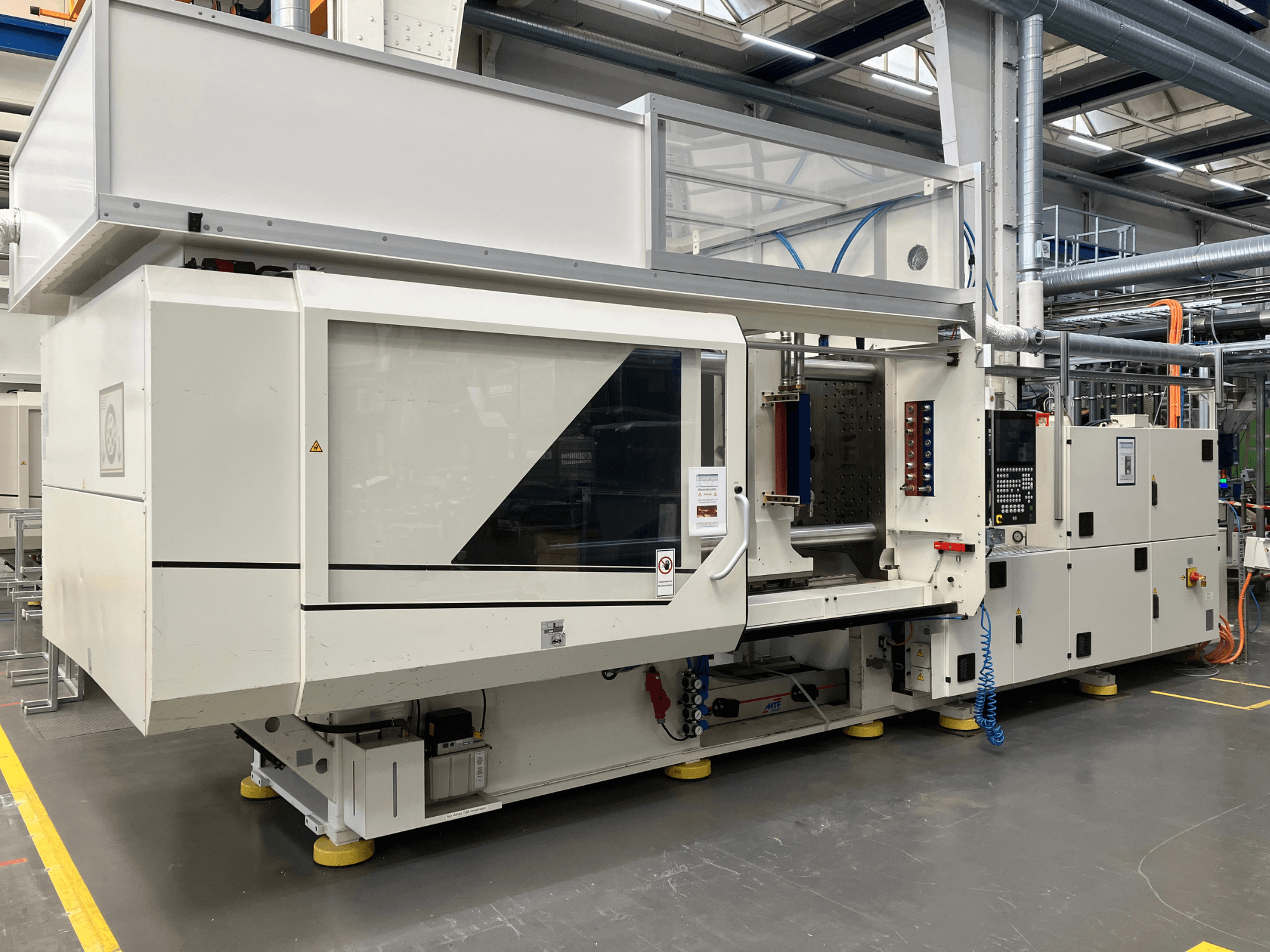 Boční pohled na vstřikovací stroj, model AET, s ovládacím panelem a průhlednými kryty, v průmyslovém prostředí.