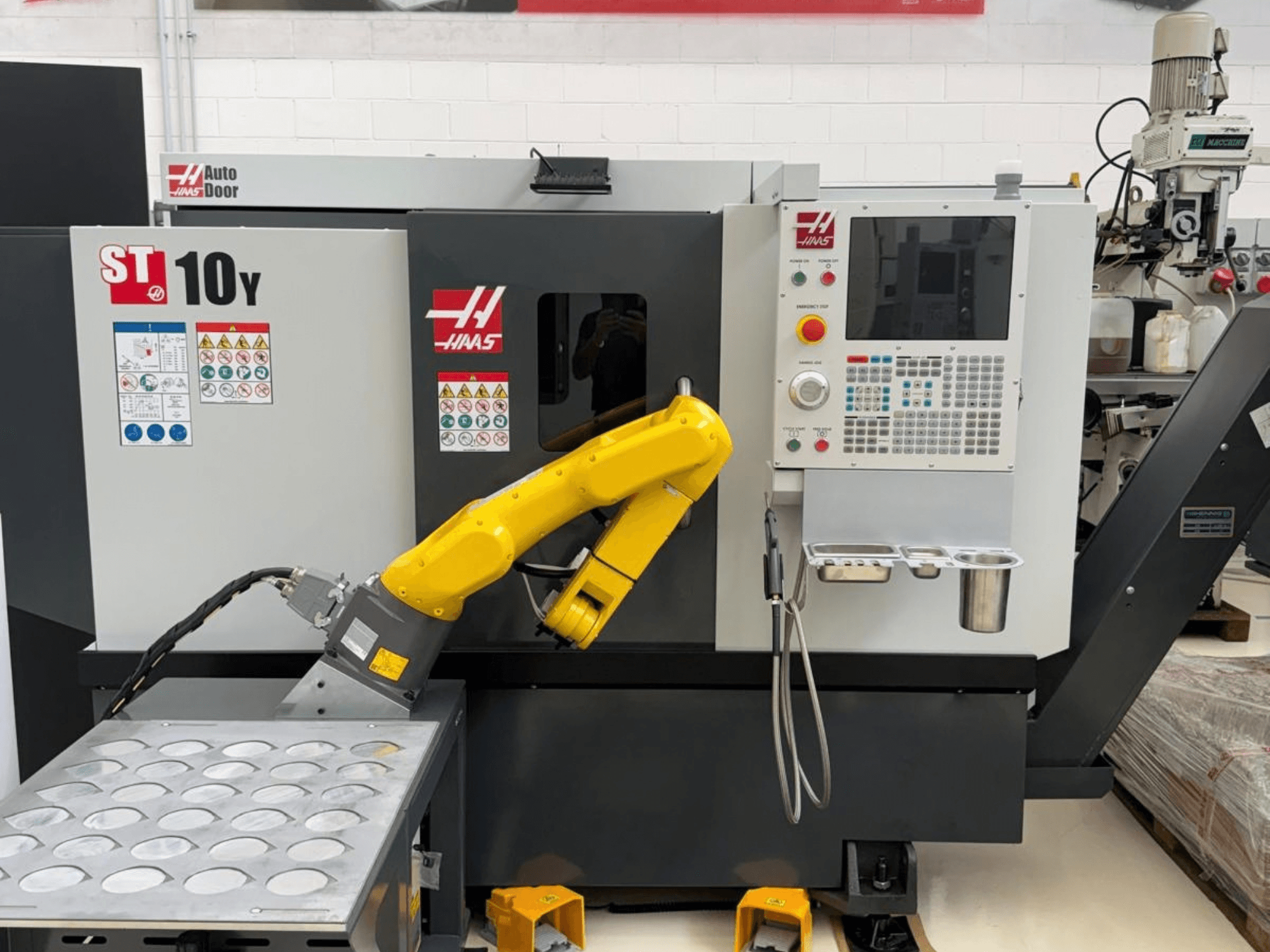 Horizontální soustruh Haas ST-10Y při pohledu zepředu, vybavený robotickým ramenem a ovládacím panelem s přihrádkami na držáky nástrojů.