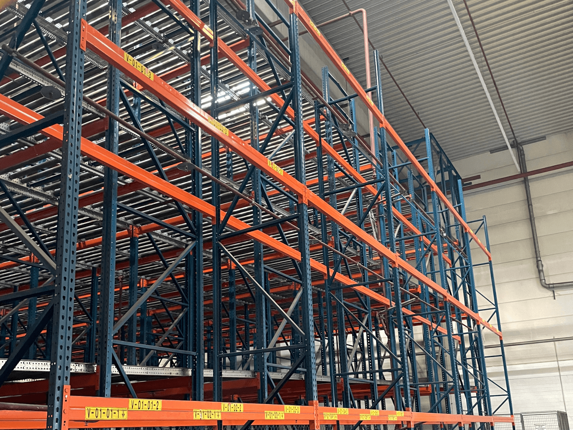 Systém FL SYSTEME F05.10 Systém FLG pro manipulaci s paletami ve skladu, zobrazený z bočního pohledu, s oranžovými a modrými regály pro vysoké zatížení.