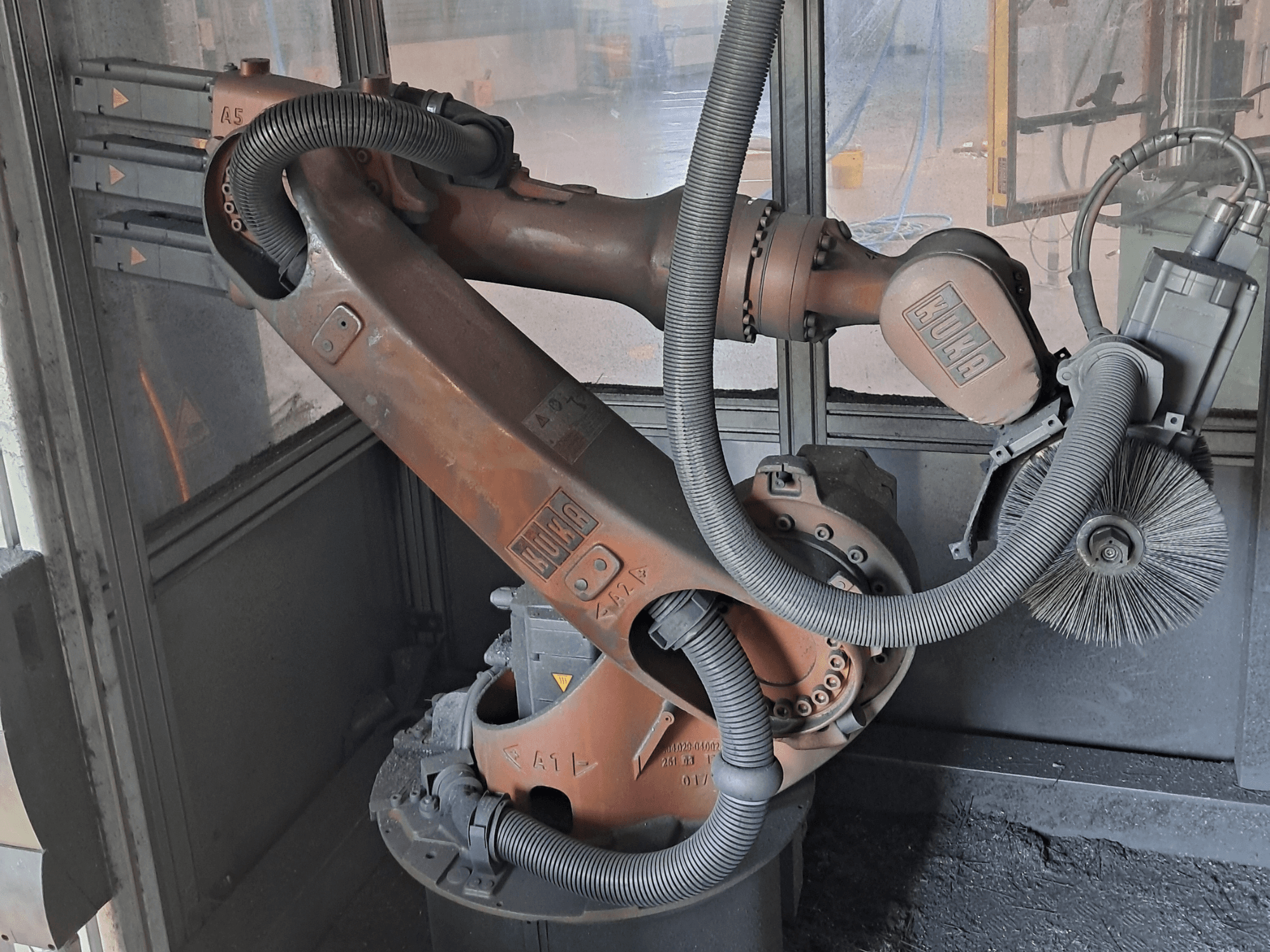 Robotické rameno KUKA KR 16-2 v bočním pohledu, na kterém jsou vidět kabely, kartáče a mechanické klouby, umístěné v pracovním prostředí.