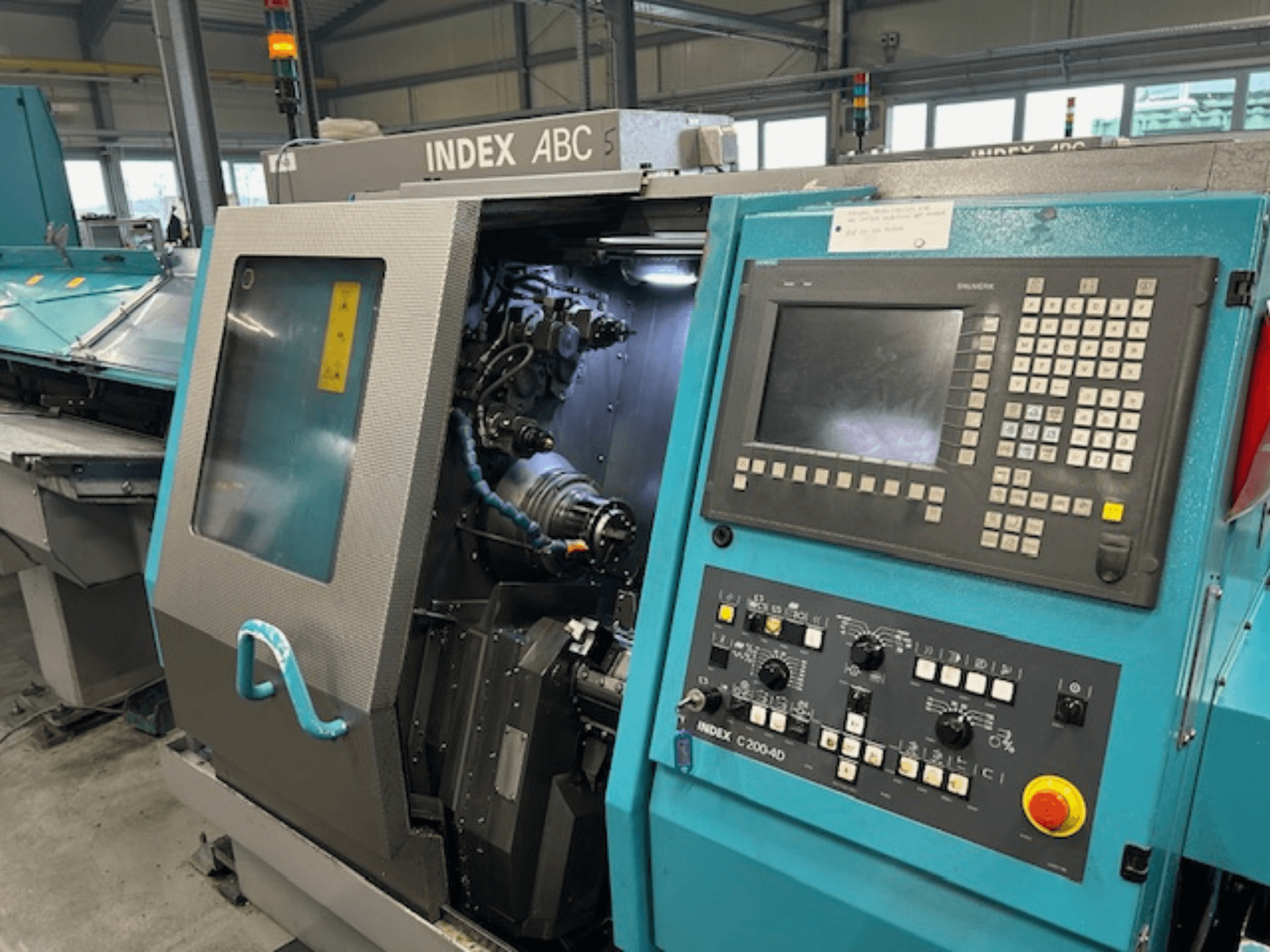 Přední pohled na CNC soustruh INDEX C200-AD s ovládacím panelem, viditelnými vnitřními součástmi a bezpečnostními prvky.