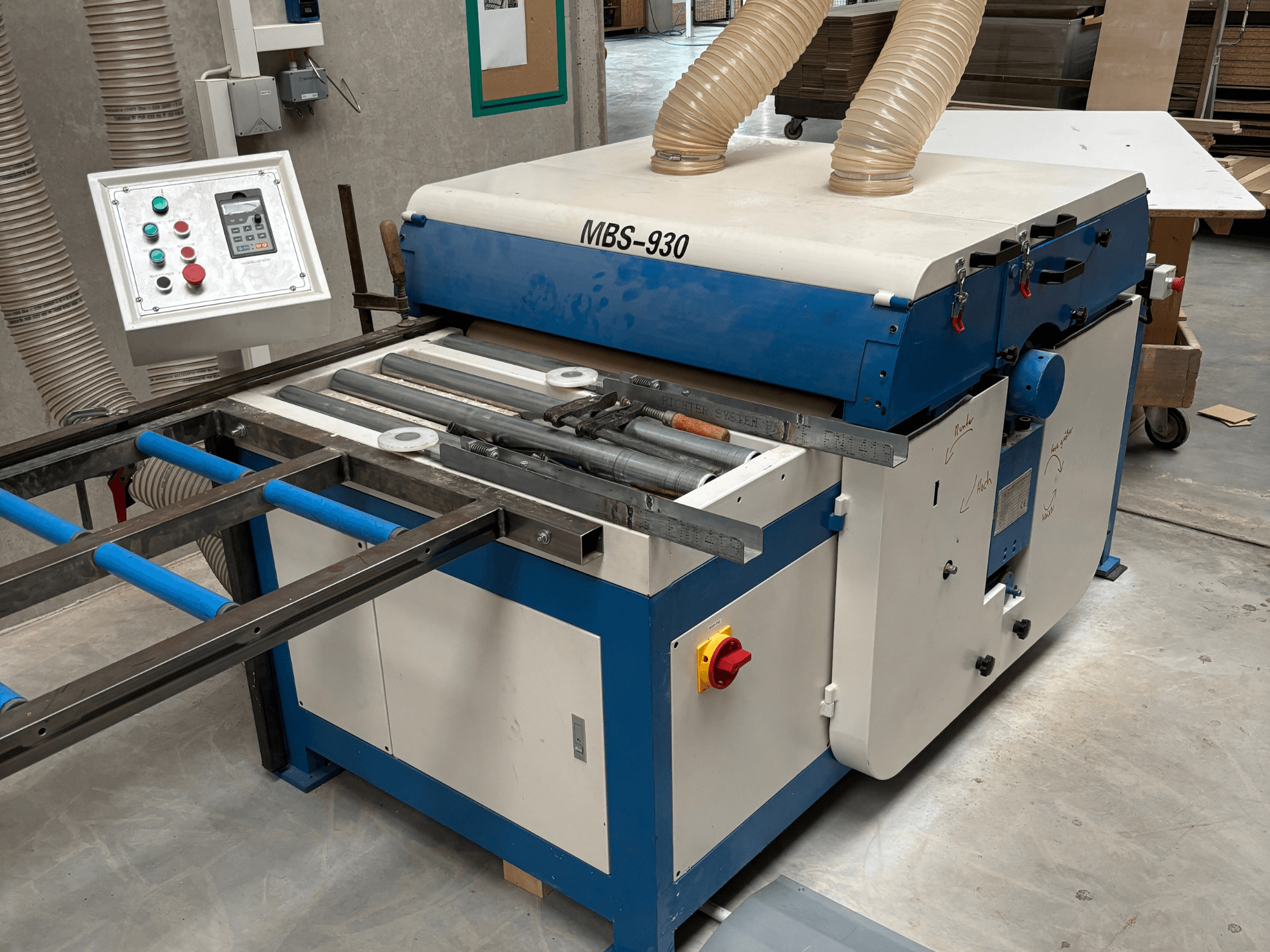 Dřevoobráběcí stroj MBS-930 s ovládacím panelem a válci, pohled z boku, s hadicemi pro odsávání prachu.