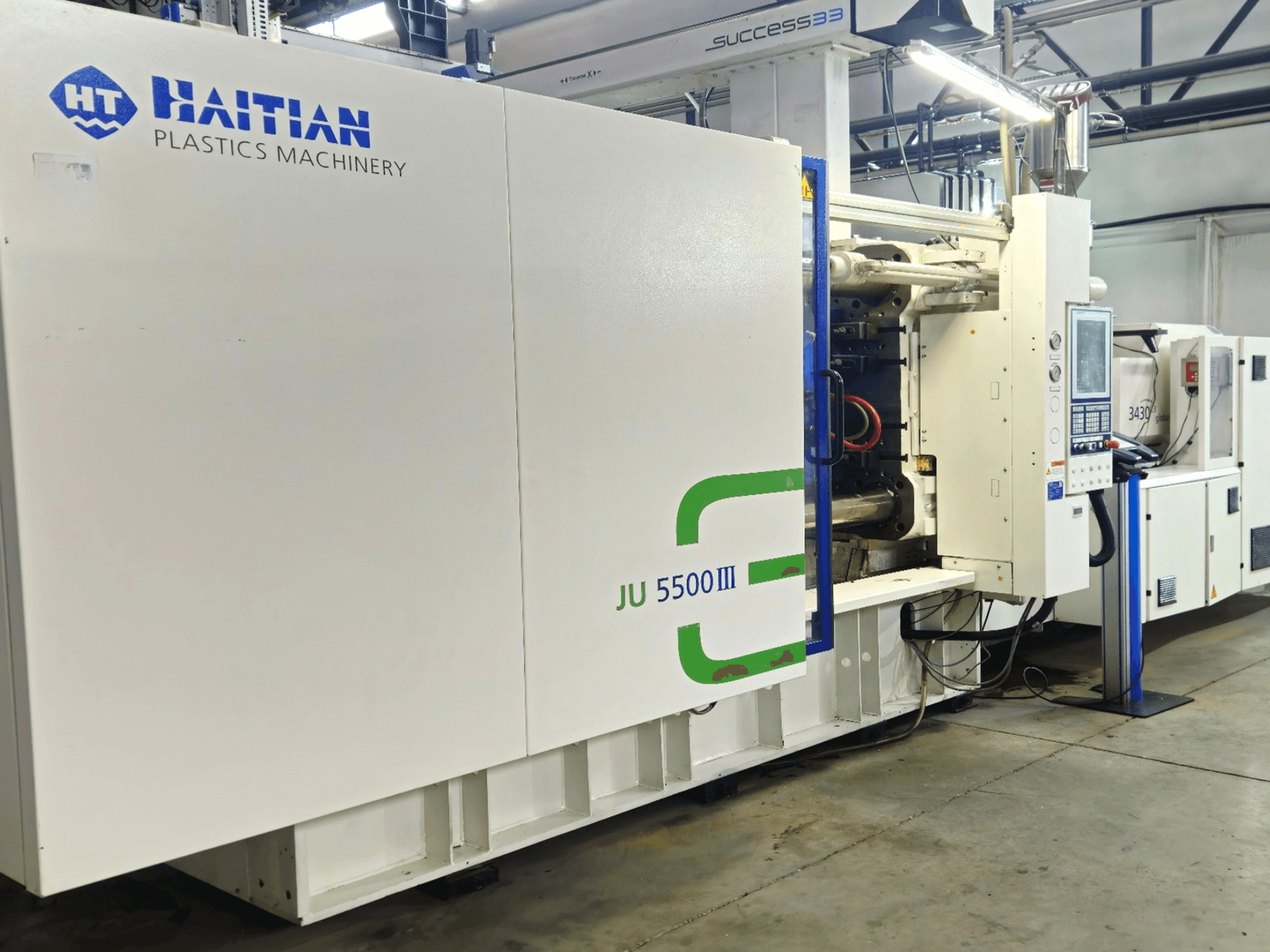 Haitský stroj na zpracování plastů JU 5500III v továrním prostředí, čelní pohled na ovládací panel a výrobní prostor.