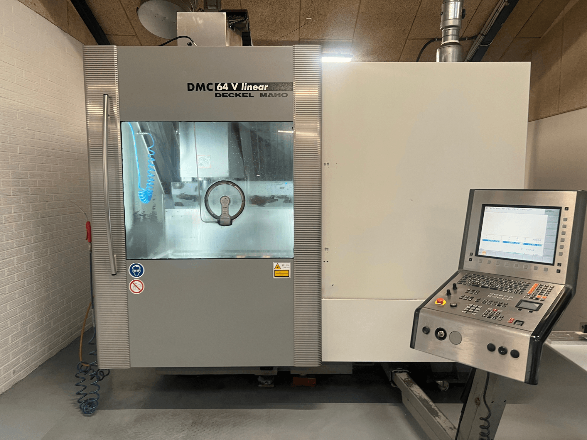 DMC 64 V Linear od Deckel Maho, čelní pohled na CNC obráběcí centrum s viditelným ovládacím panelem a tryskou chladicí kapaliny.