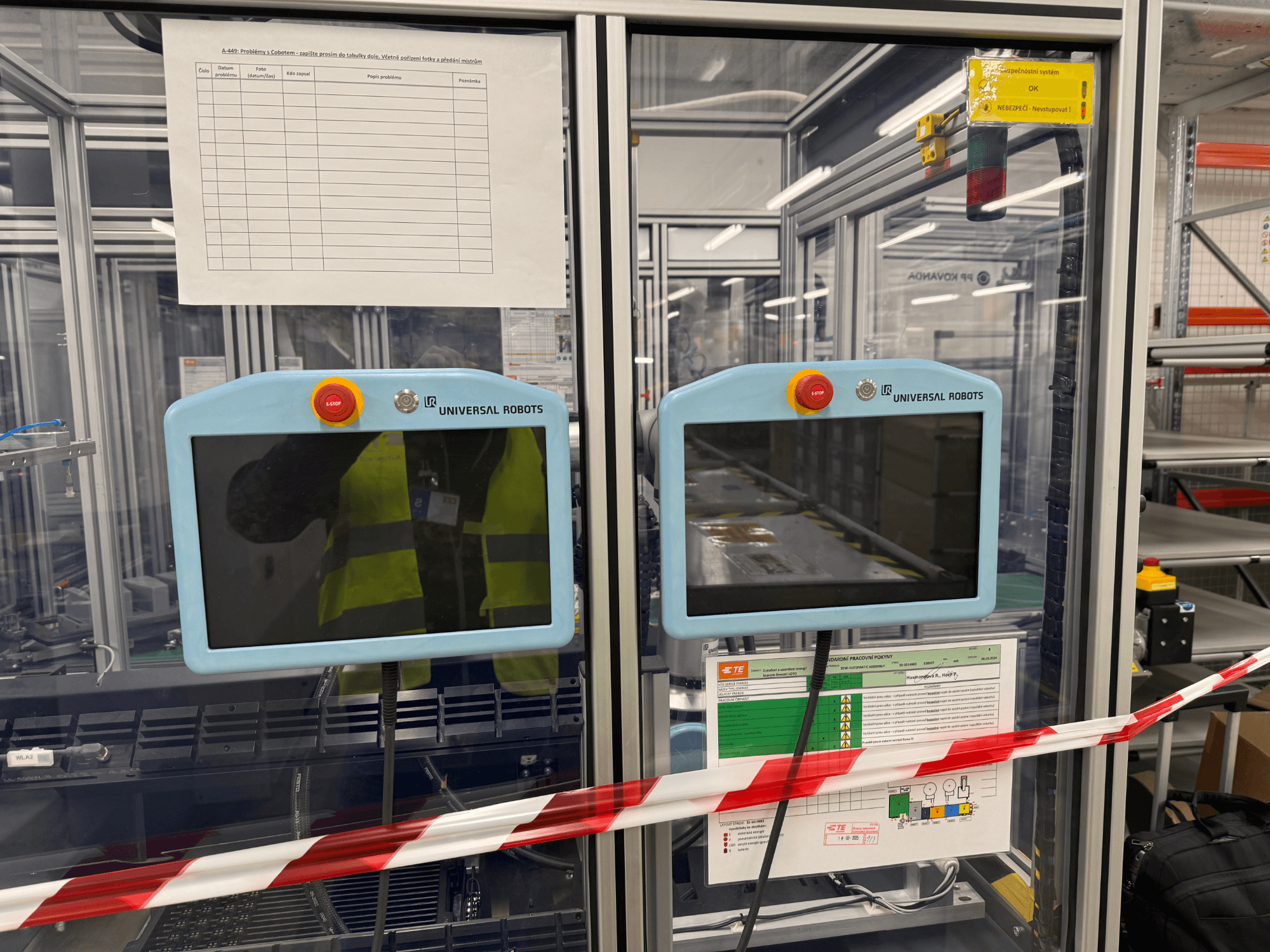 Ovládací panel pro robotické rameno Universal Robots UR5 e se dvěma monitory, tlačítky nouzového zastavení a bezpečnostními pokyny.