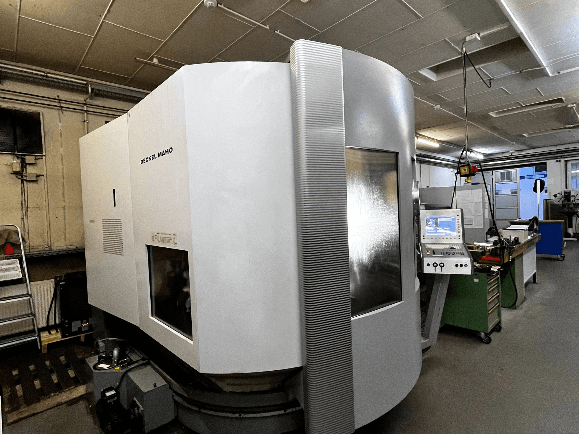 Stroj Deckel Maho CNC, pohled zepředu, bílý exteriér, viditelný ovládací panel, dílenské nastavení.