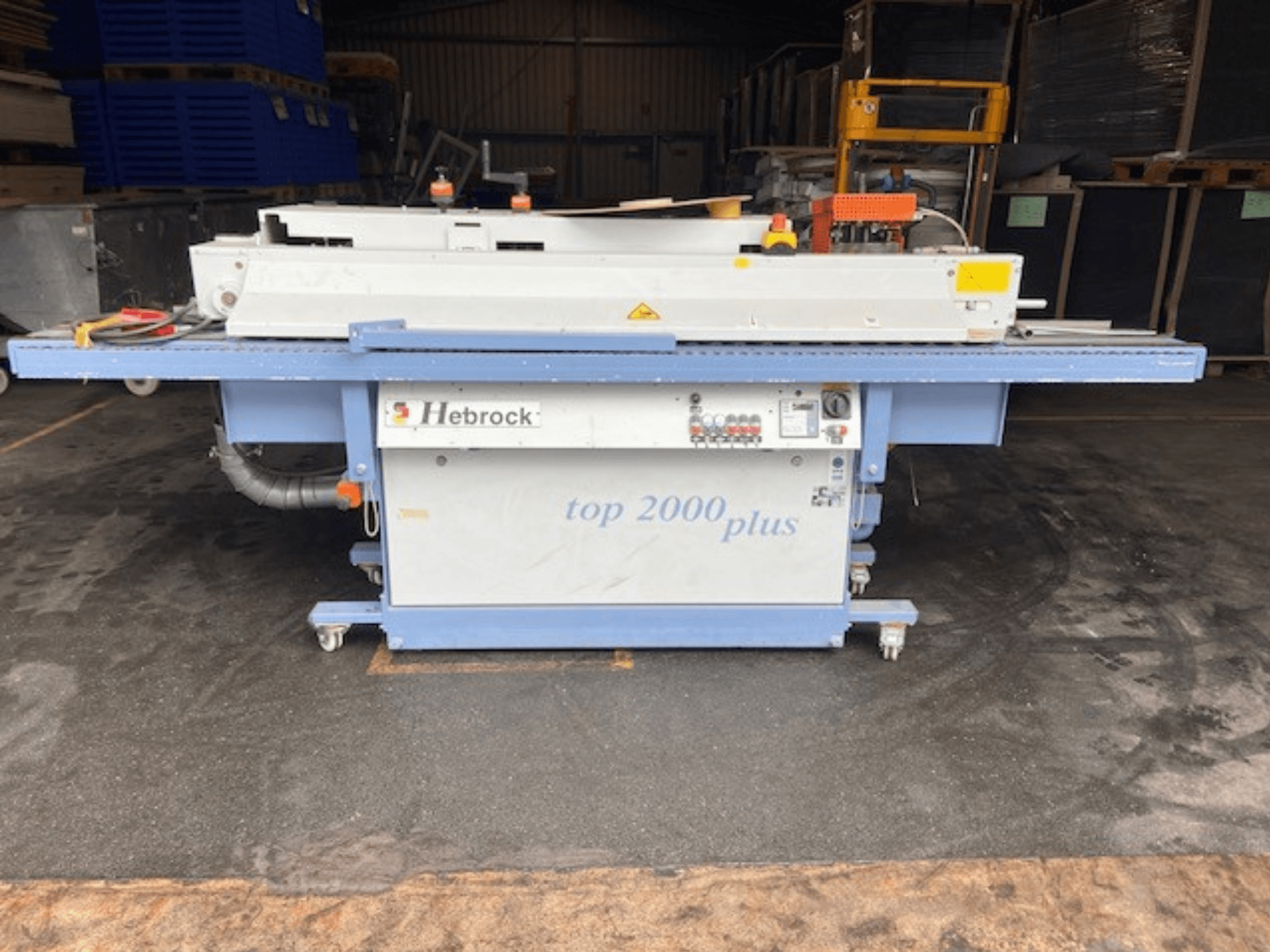 Hebrock Top 2000 Plus, pohled zepředu; průmyslový elektrický stroj s ovládacím panelem, kolečky pro mobilitu a viditelnými bezpečnostními štítky.