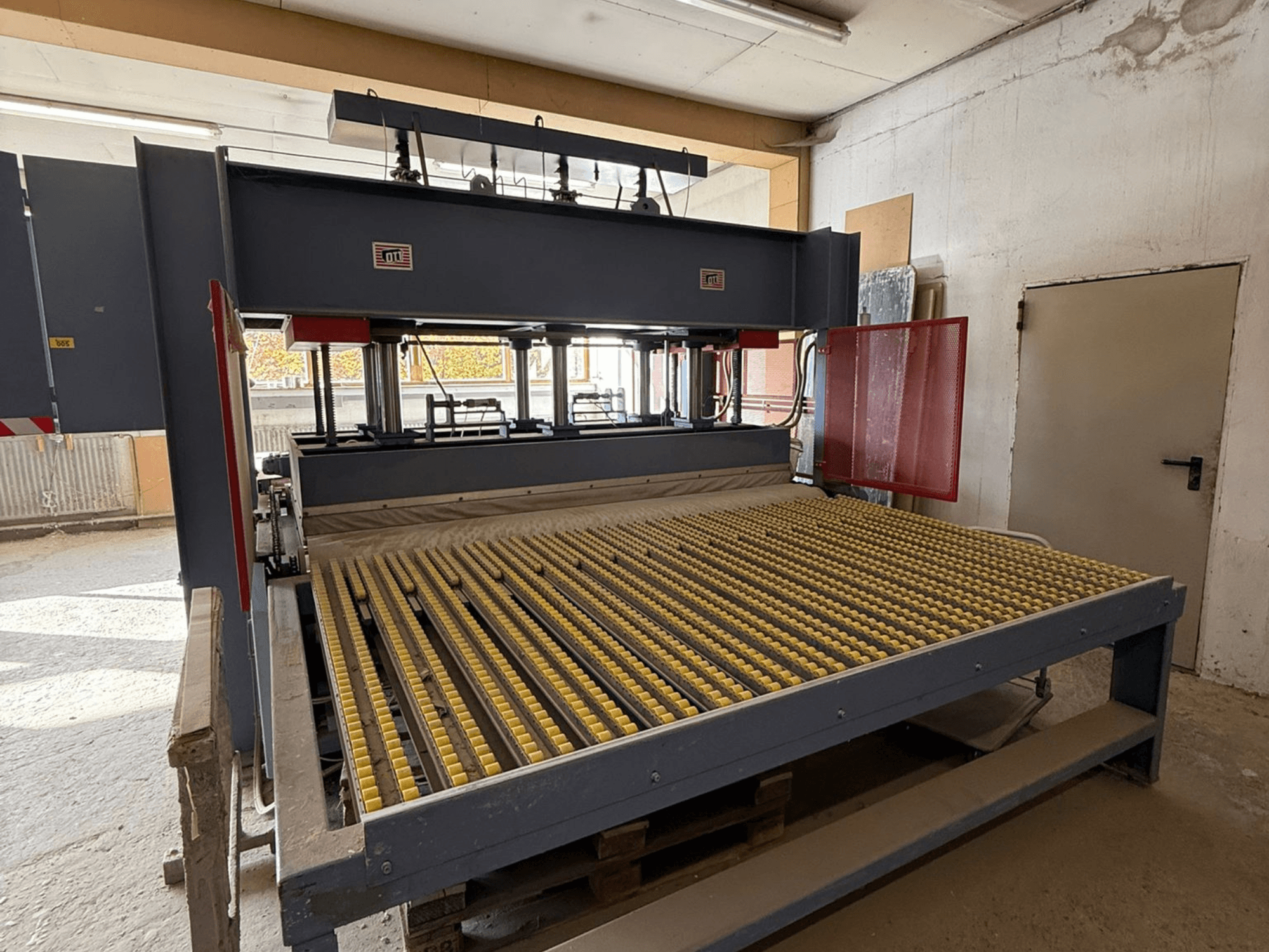 Průmyslový stroj se žlutými válci, pohled zepředu, viditelné logo značky, používaný ke zpracování materiálů v dílně.