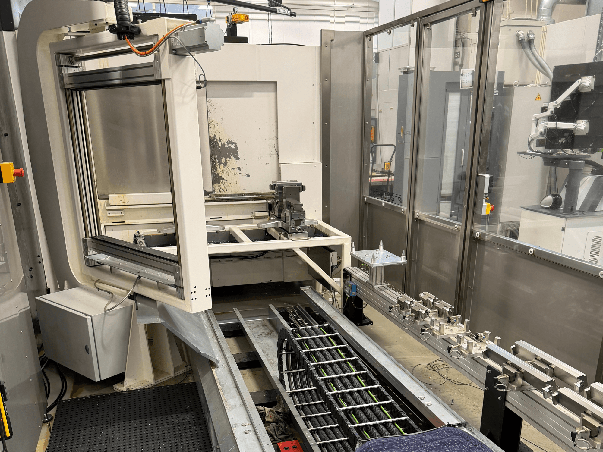 Automatizované průmyslové pracoviště s robotickým ramenem, kolejnicovým systémem a ovládacím panelem v bočním pohledu.