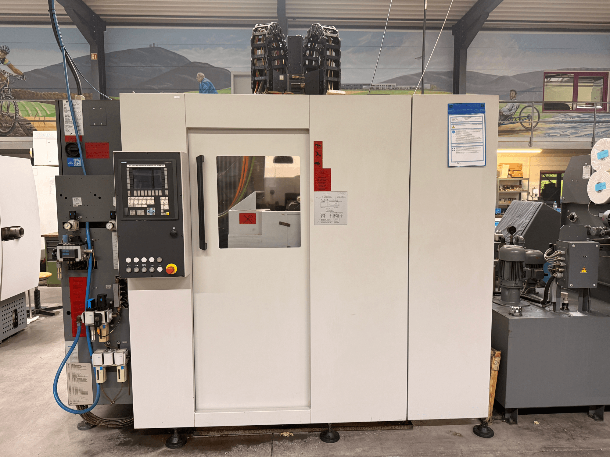 Bílé CNC obráběcí centrum s ovládacím panelem, pohled zepředu, s tlačítky a digitálním displejem, v dílenském prostředí.