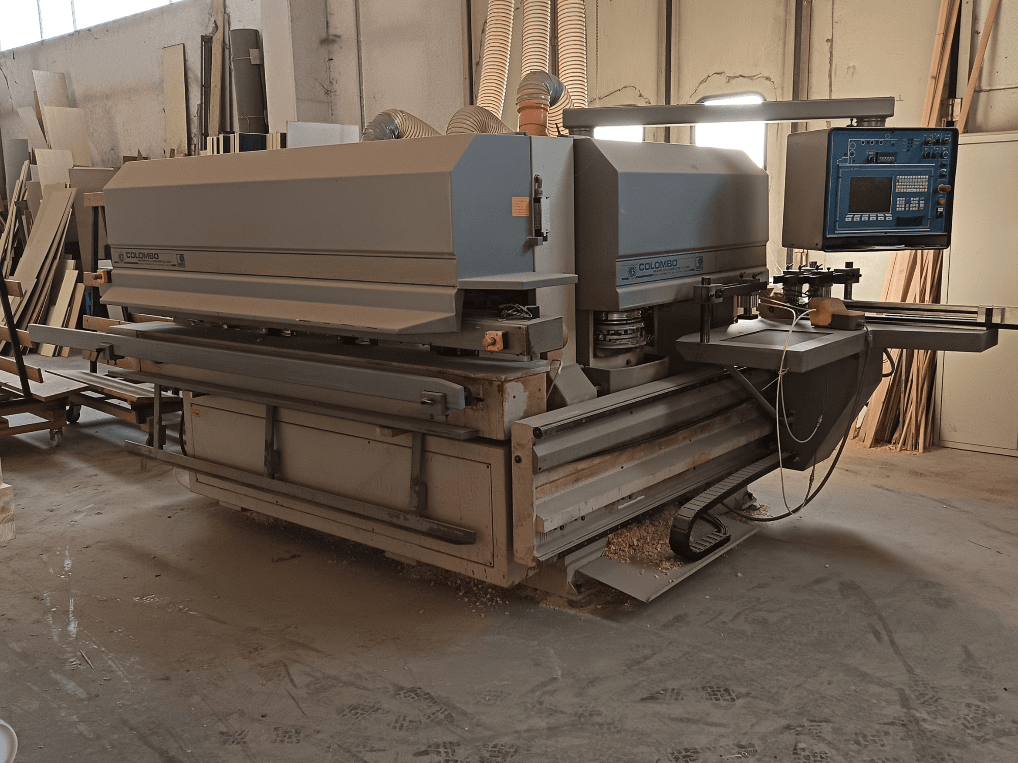 Dřevoobráběcí stroj Colombo, boční pohled na ovládací panel, řezné kotouče a hromadění pilového prachu v dílně.