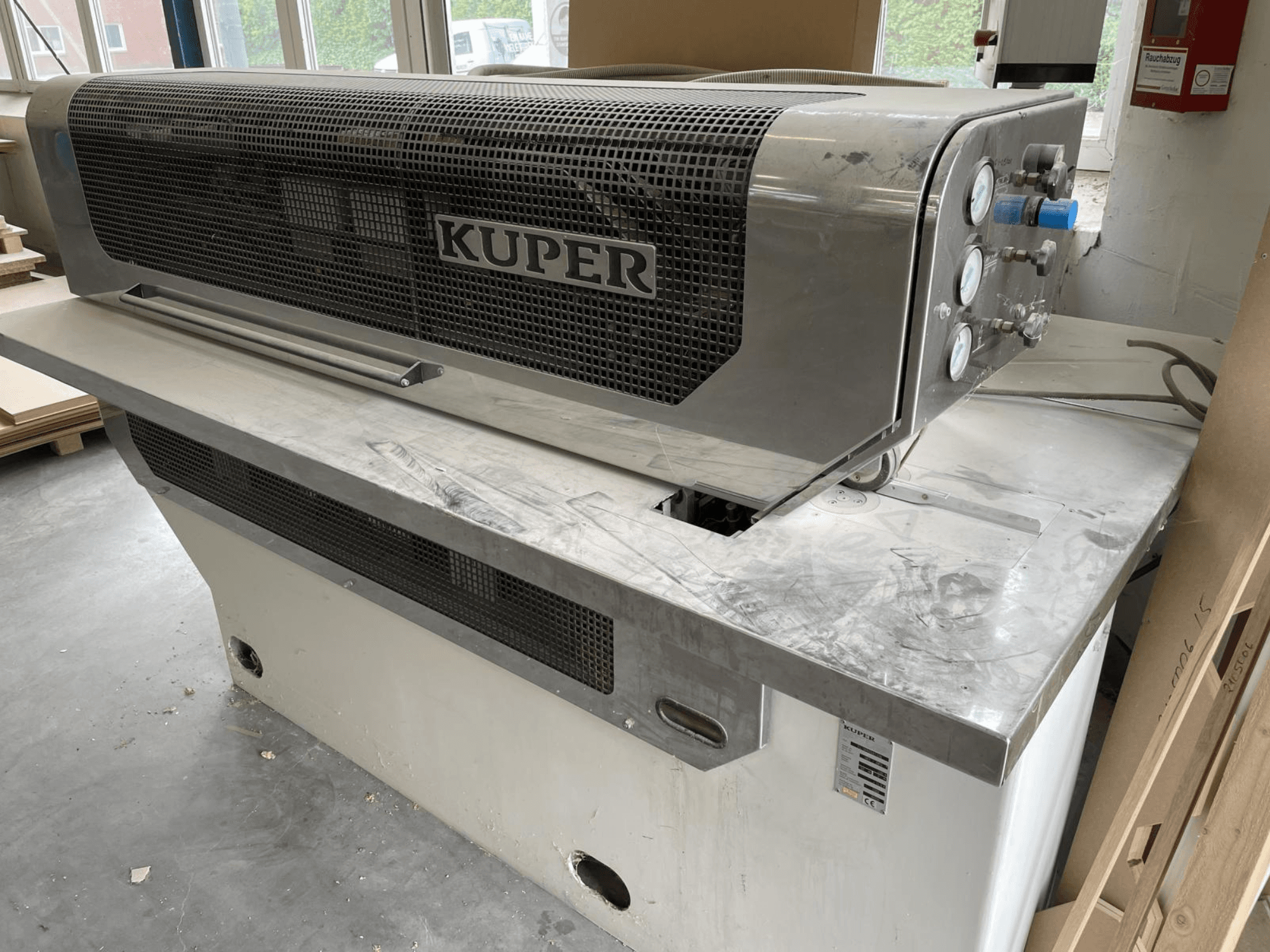 Gilotina na dýhy KUPER FLI, pohled zepředu, s tělem z nerezové oceli, měřidly a čistou řeznou plochou na pracovním stole.