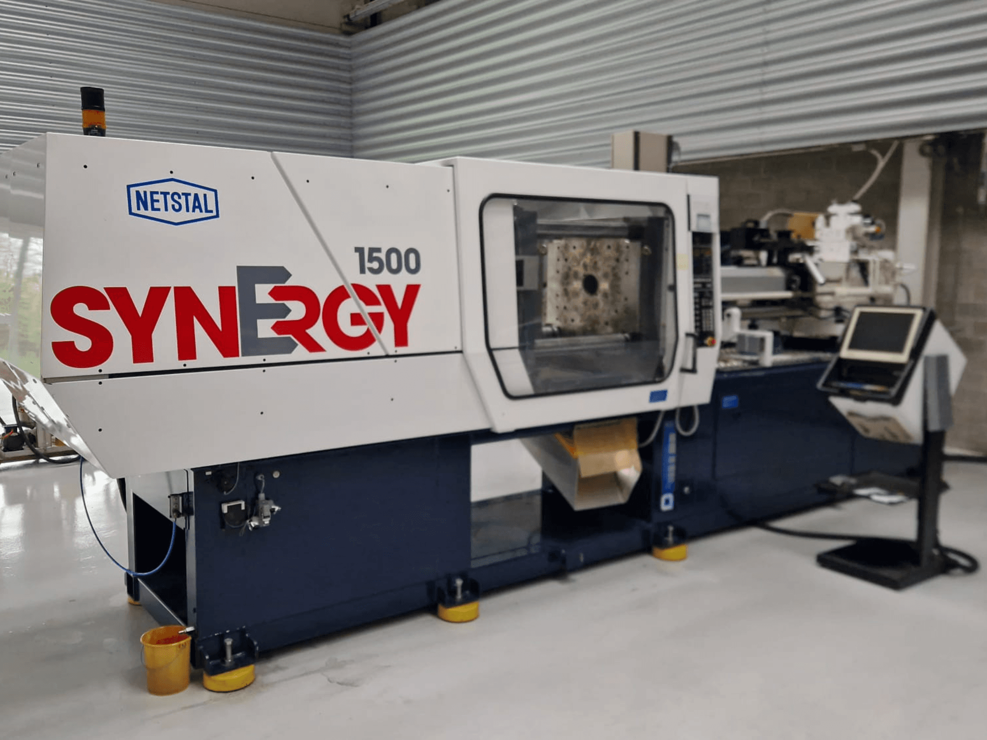 Hydraulický vstřikovací stroj Netstal Synergy 1500-460, pohled zepředu na ovládací panel a otevřený vstřikovací prostor.