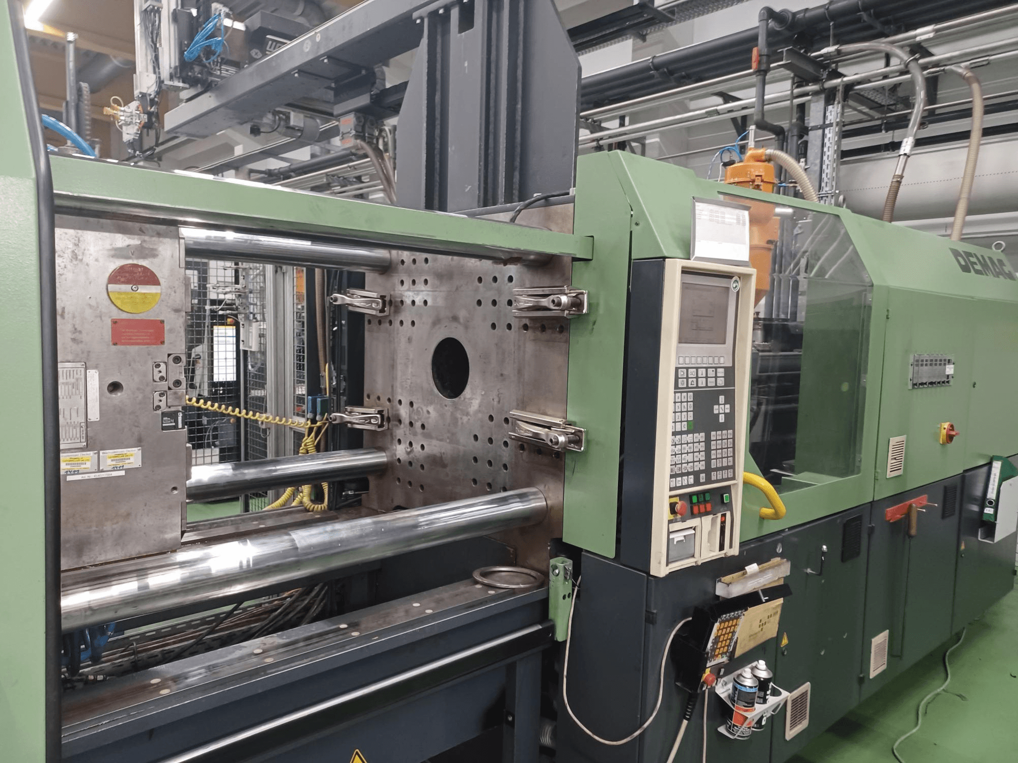 Vstřikovací stroj Demag, pohled zepředu, s ovládacím panelem, kovovými hydraulickými válci a bezpečnostními prvky.
