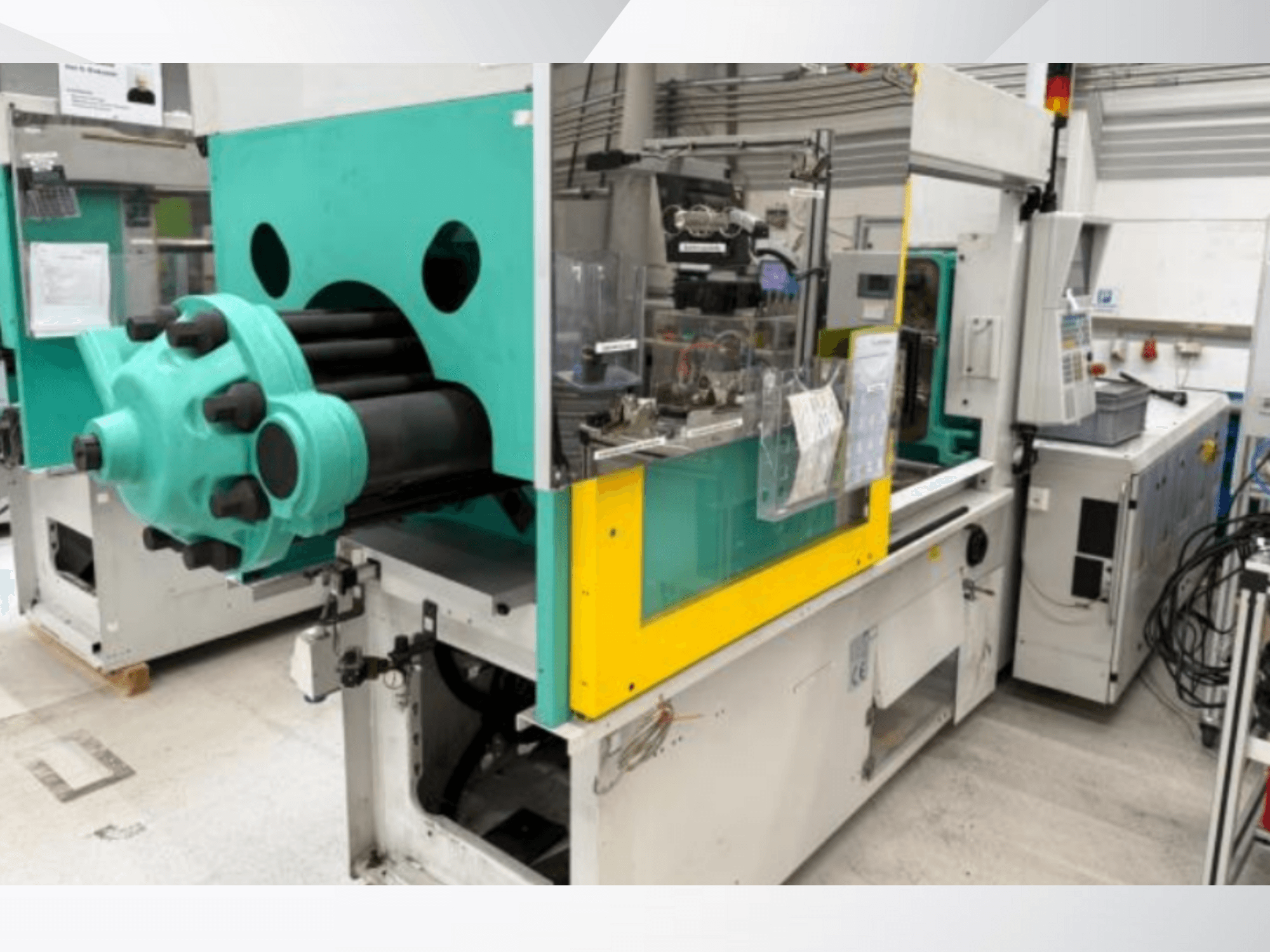 Vstřikovací stroj, světle modrý a žlutý, pohled zepředu, s viditelnou formou a ovládacím panelem se štítky.