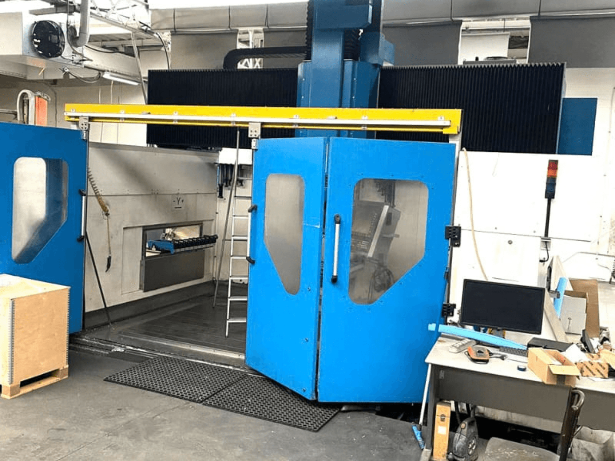 Pohled zepředu na vertikální obráběcí centrum TECHMILL LABOR SHAPE 3220 s otevřenými modrými dvířky, za nimiž je vidět vnitřní pracovní prostor.