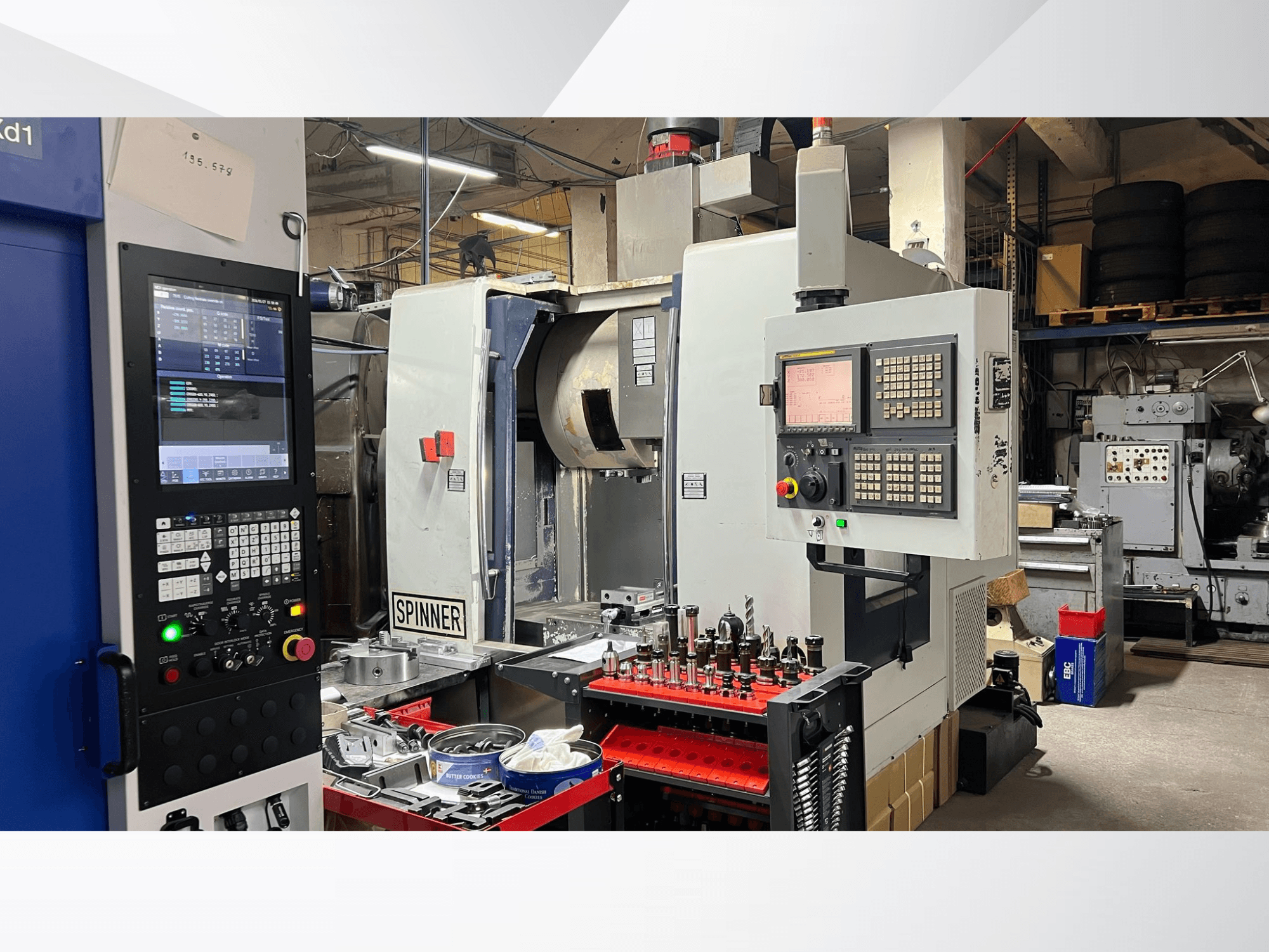 CNC stroj s viditelným ovládacím panelem, nástroji a obrobky při pohledu zepředu v dílenském prostředí.