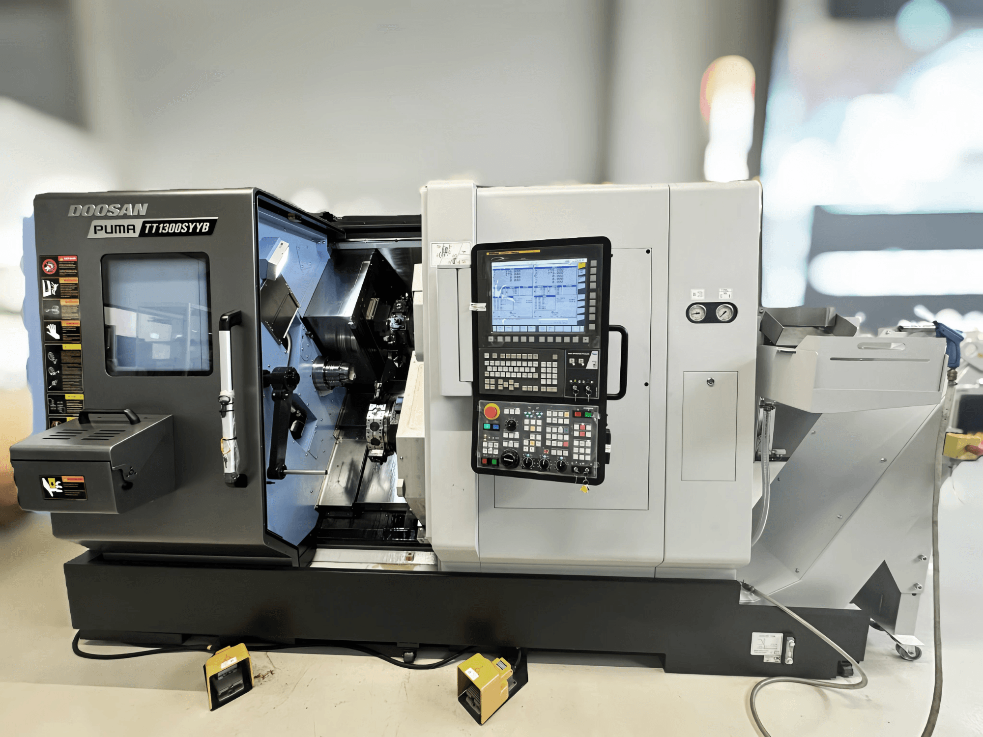 Soustružnické centrum Doosan Puma TT1300SYYB v bočním pohledu, ukazuje ovládací panel a vnitřní prostor stroje s viditelnými nástroji.