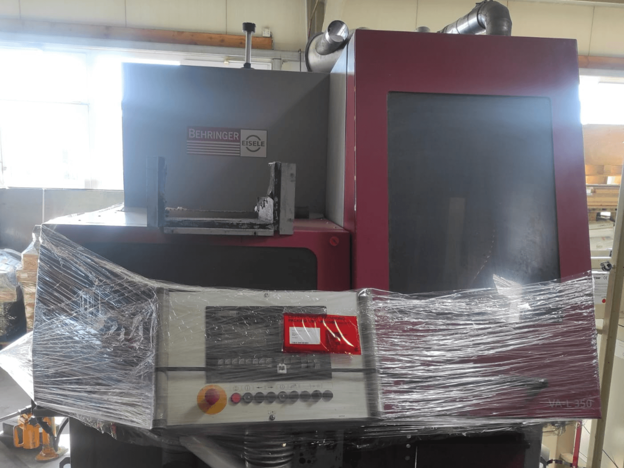 Stroj Behringer Eisele VA L 560, pohled zepředu, zabalený v plastu, s viditelným ovládacím panelem a tlačítky.