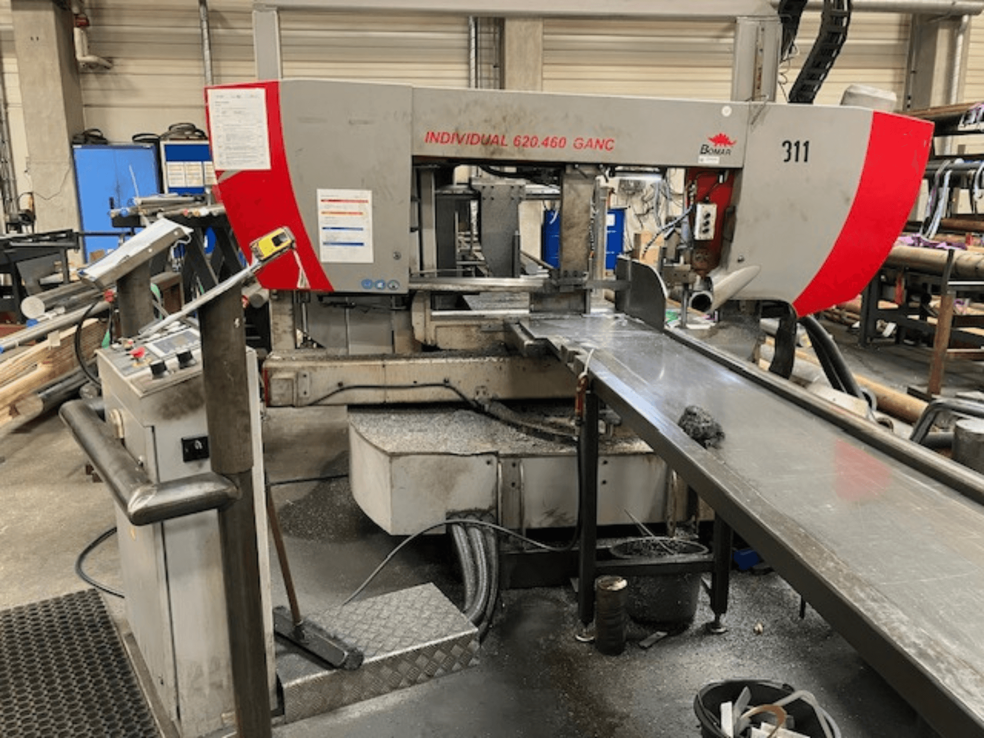 Pásová pila BOMAR INDIVIDUAL 620-460 GANC, pohled zepředu, zobrazující ovládací prvky, řezný prostor a pozadí průmyslové dílny.