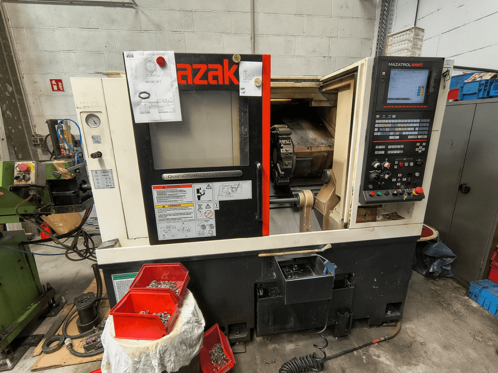 Mazak Quick Turn Smart 100 S, boční pohled znázorňující ovládací panel, vaničku na chladicí kapalinu a úložné přihrádky se šrouby.