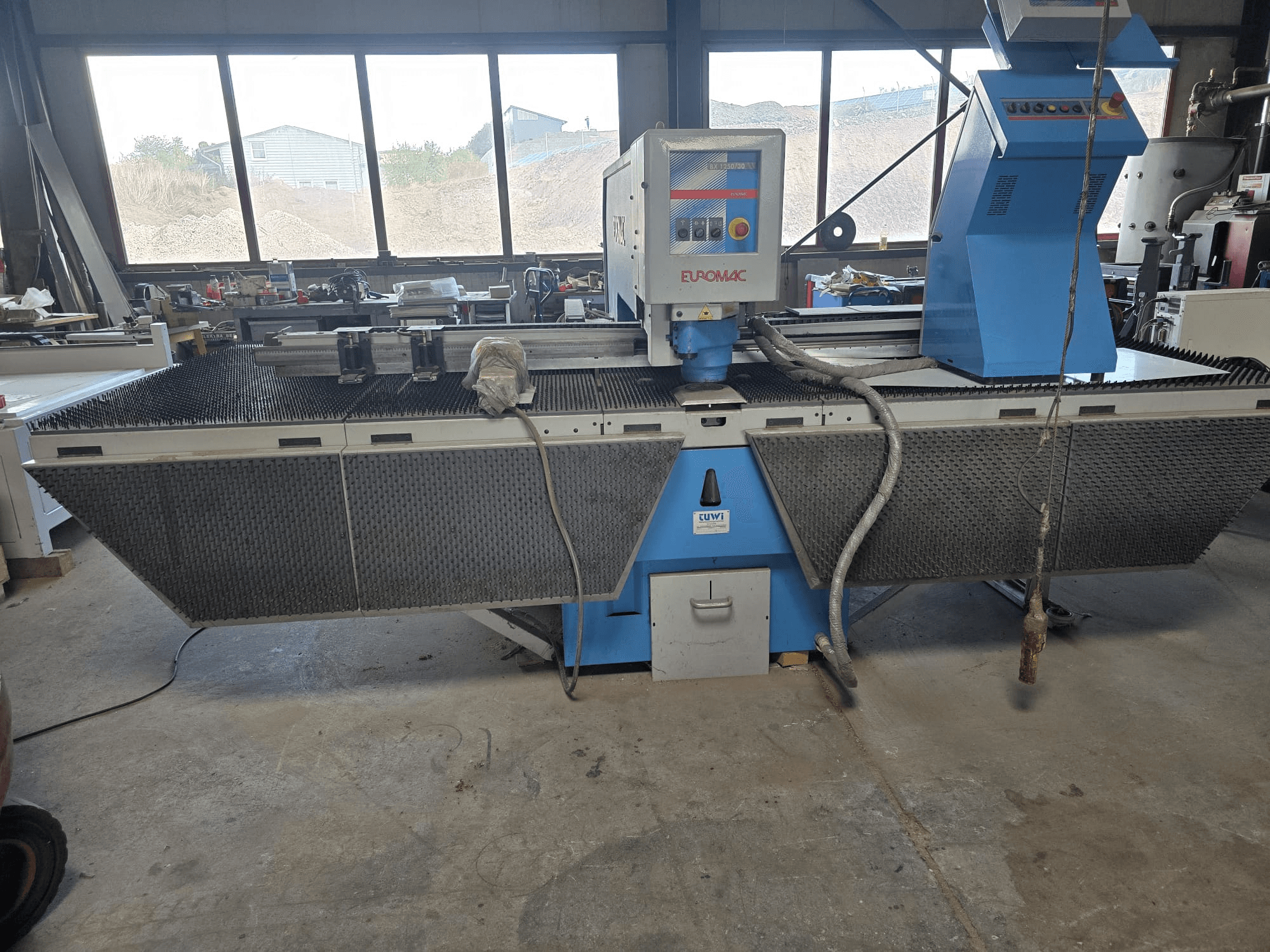 CNC děrovací stroj Euromac BX 1250/30 v dílně, boční pohled znázorňující ovládací prvky stroje, průmyslový design a pracovní stůl pro řezání kovů.