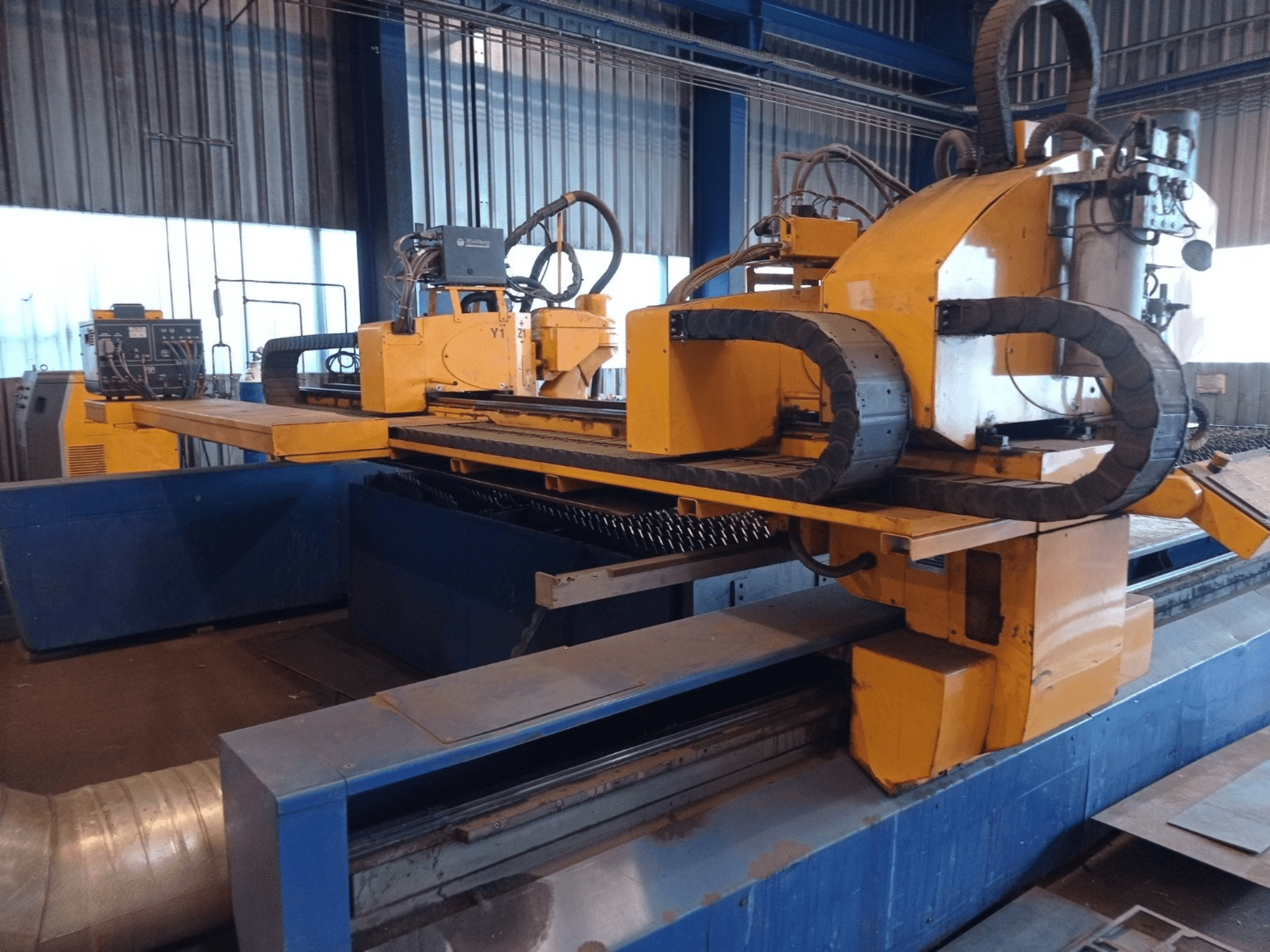 Žlutý CNC plazmový řezací stroj se dvěma horizontálními rameny, zobrazený zepředu, s ovládacím panelem a řezacím ložem.