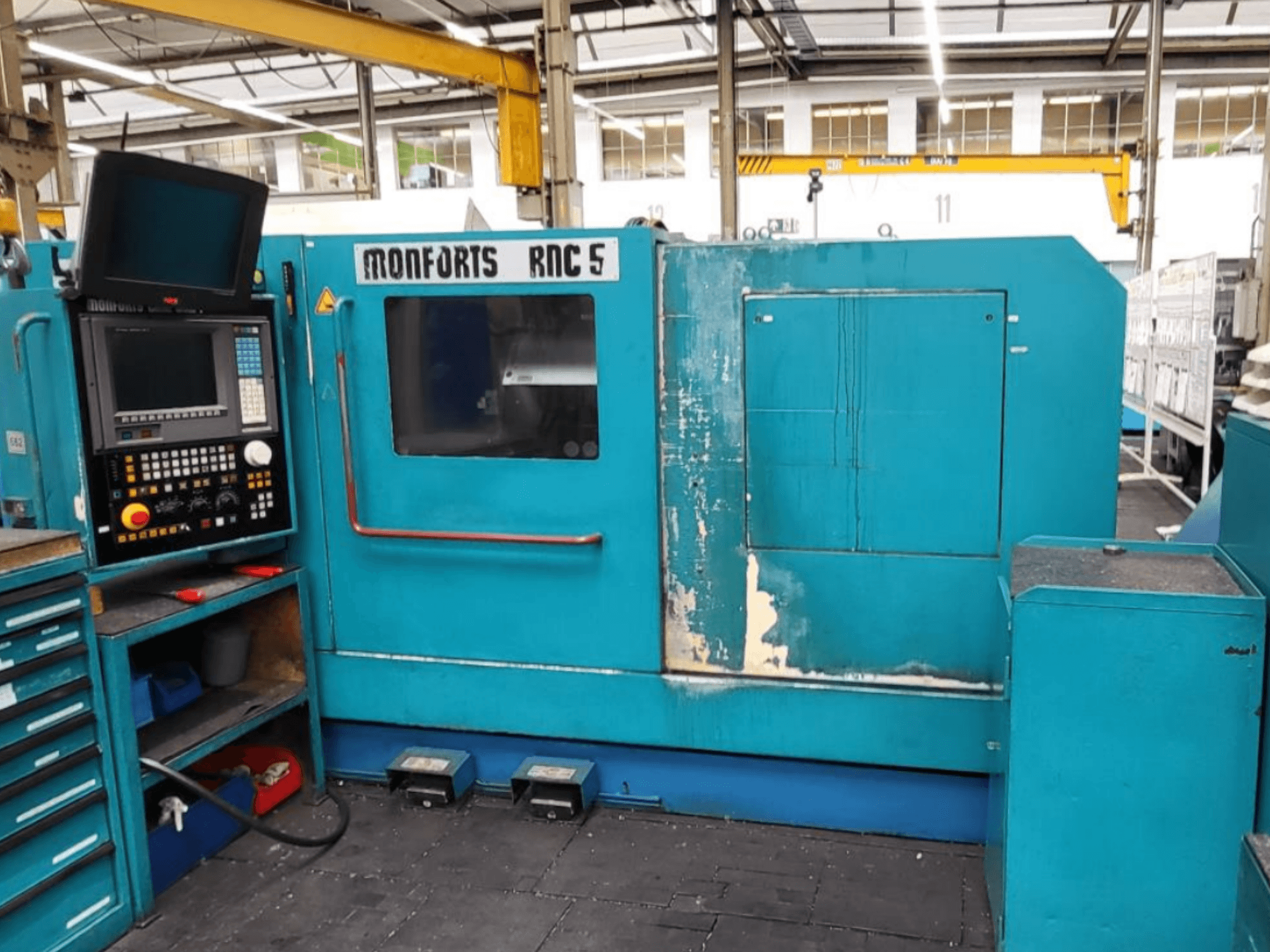 Pohled zepředu na horizontální soustruh Monforts RNC 5 s ovládacím panelem, modrým vnějším povrchem a viditelnými stopami opotřebení.
