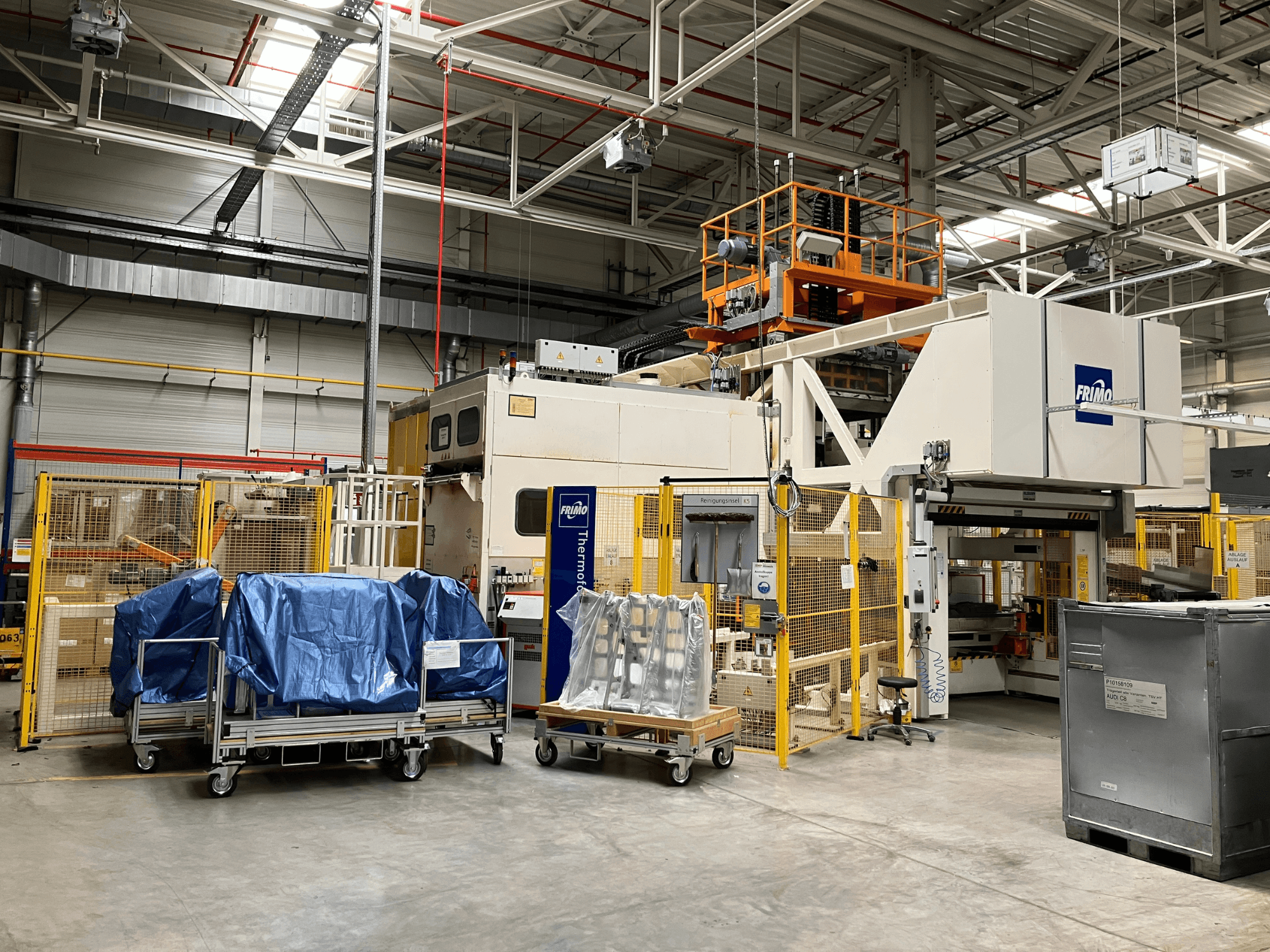 Stroj na zpracování plastů FRIMO FTL 80/200 Fullflex v továrně, pohled zepředu s viditelnými modrými plachtami a bezpečnostními zábranami.