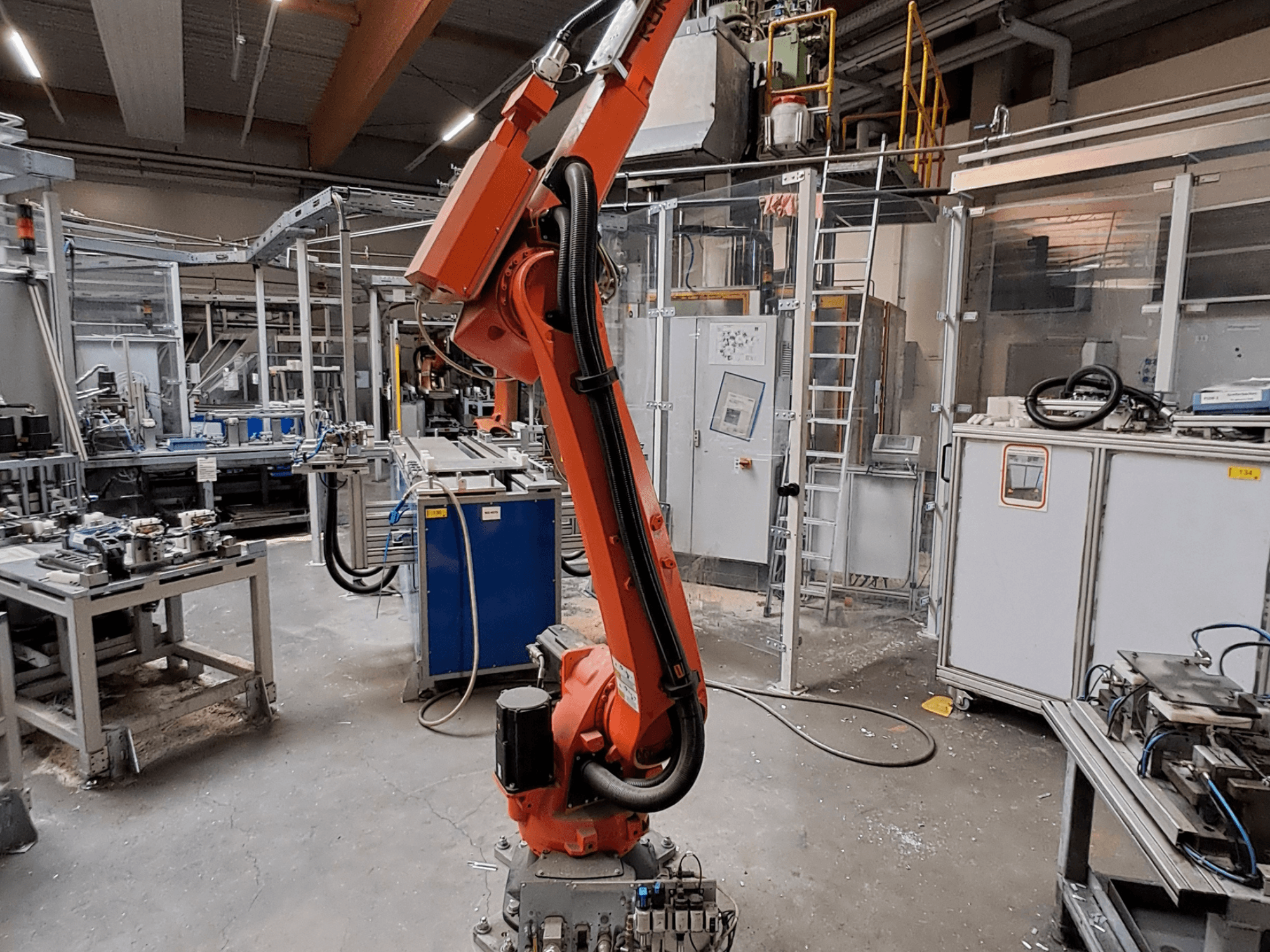 Robotické rameno KUKA KR 26 R3100/SEL v průmyslovém prostředí, zobrazené z bočního pohledu s provozním zařízením v pozadí.