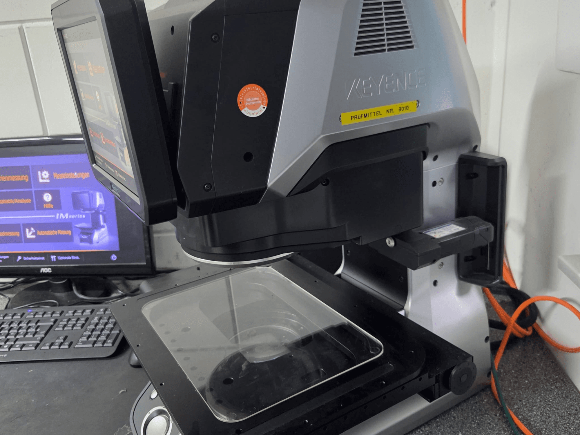 Optický měřicí stroj KEYENCE IM 7030, pohled zepředu s dotykovým displejem a skleněnou měřicí deskou.