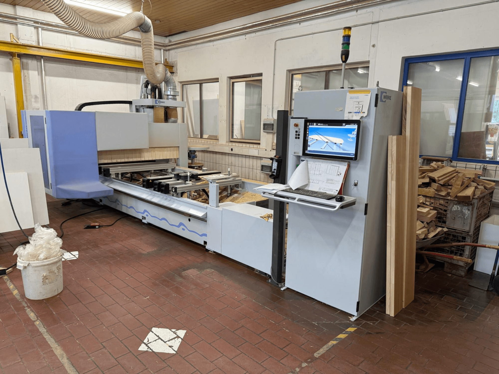 CNC centrum pro obrábění dřeva Weeke PROFI BMG211/32/12/K, pohled zepředu, s ovládacím panelem a kusy dřeva, vybavené systémem odsávání prachu.