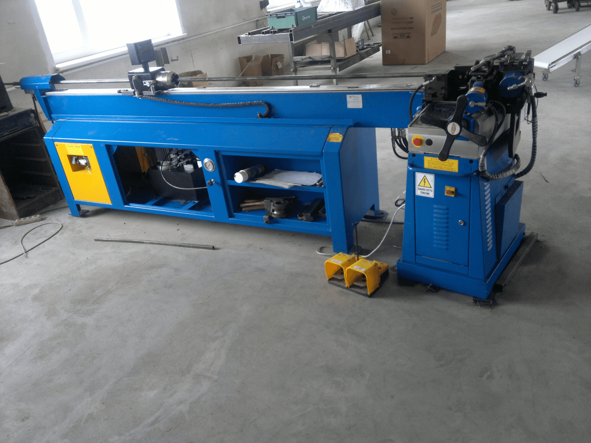 Modrý dřevoobráběcí stroj se žlutými akcenty, boční pohled; má ovládací panel, nožní pedály a sestavu otočných nožů.