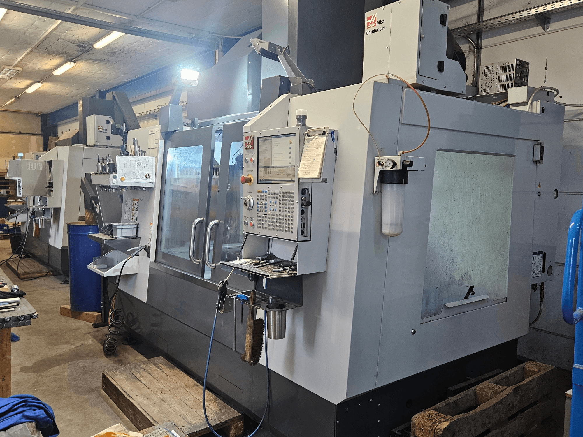 Vertikální obráběcí centrum Haas VF-3YT/50 v dílně, pohled zepředu na ovládací panel, držáky nástrojů a kondenzátor mlhy.