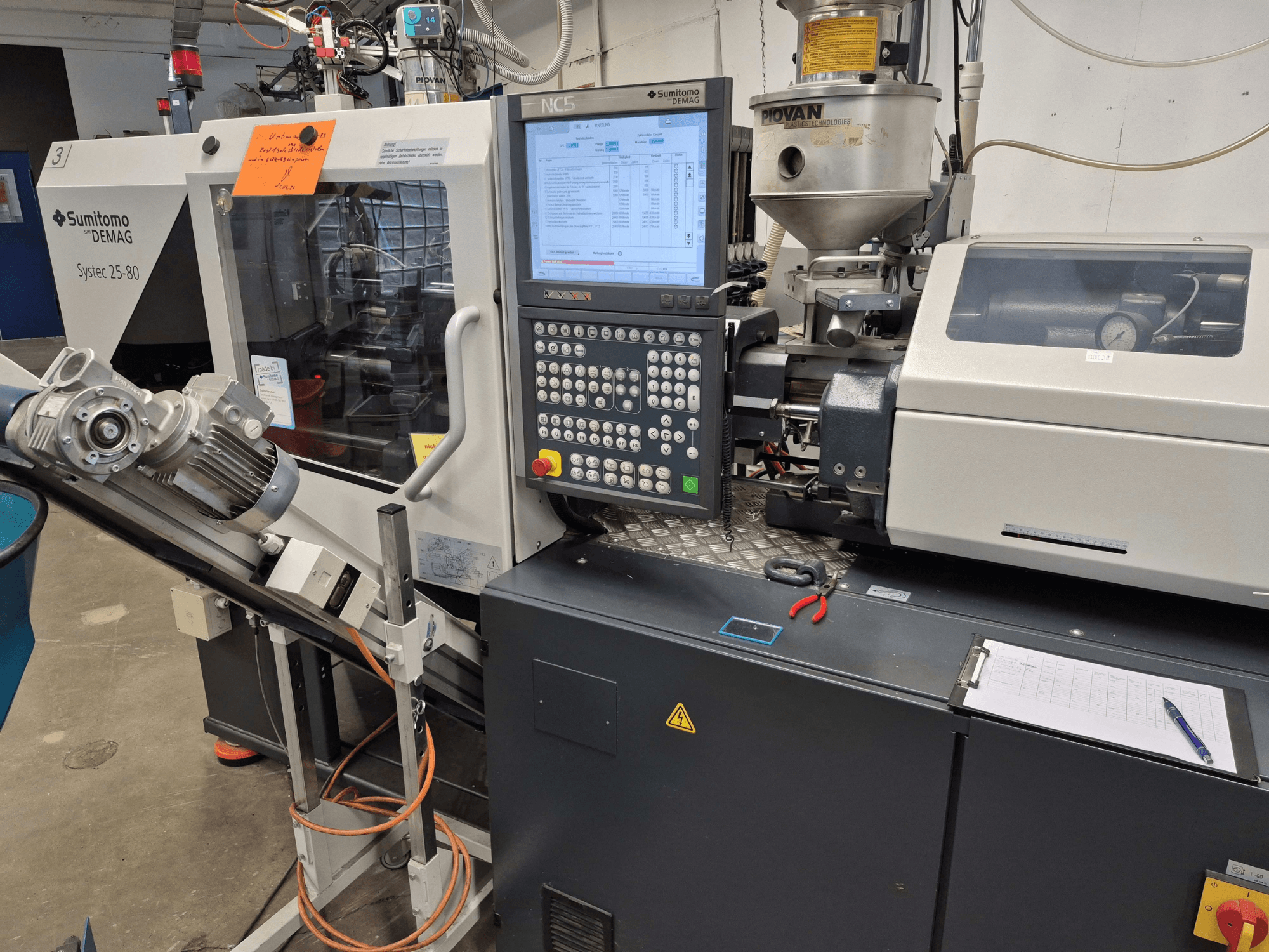 Hydraulický vstřikovací lis SUMITOMO SHI DEMAG Systec 25/320-80, pohled zepředu s viditelným ovládacím panelem a podávacím systémem.