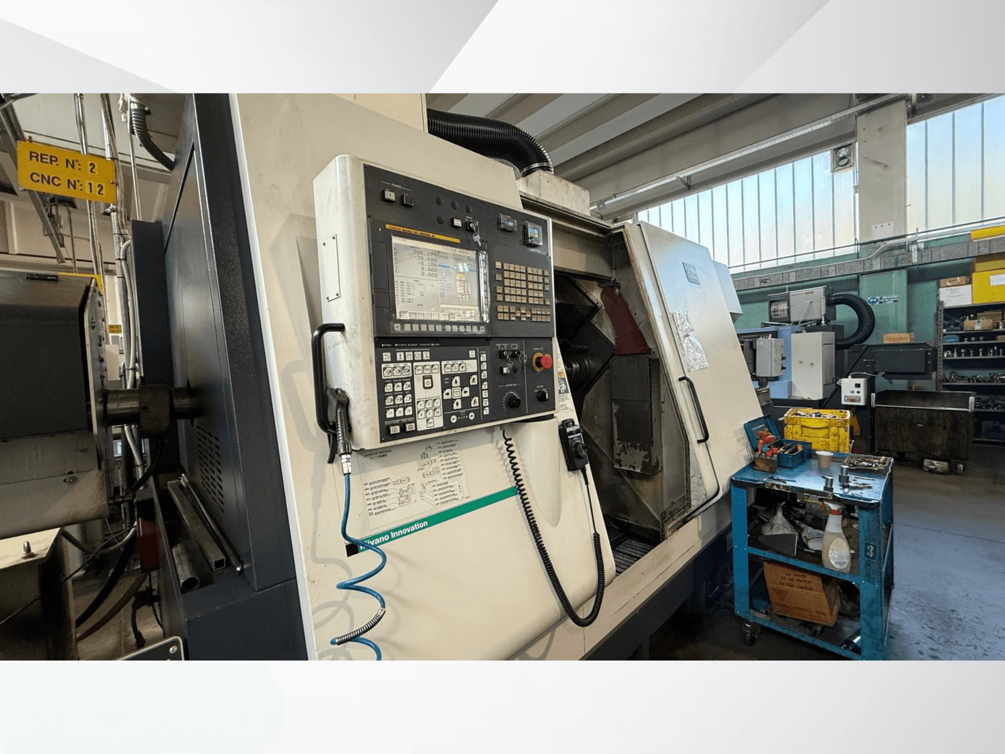 Pohled zepředu na horizontální soustruh Miyano ABX64 YY2 s ovládacím panelem, s nástroji a vybavením v dílně.